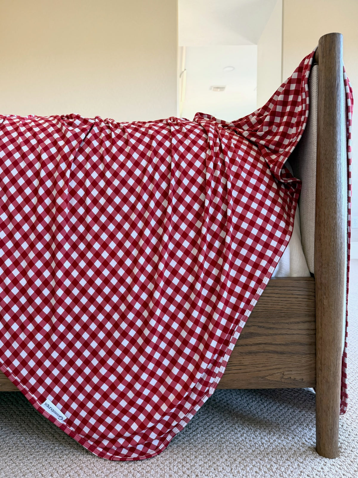 A luxurious red and white gingham ckeckin’ it twice bamboo blanket draped over the foot of a wooden bed frame.