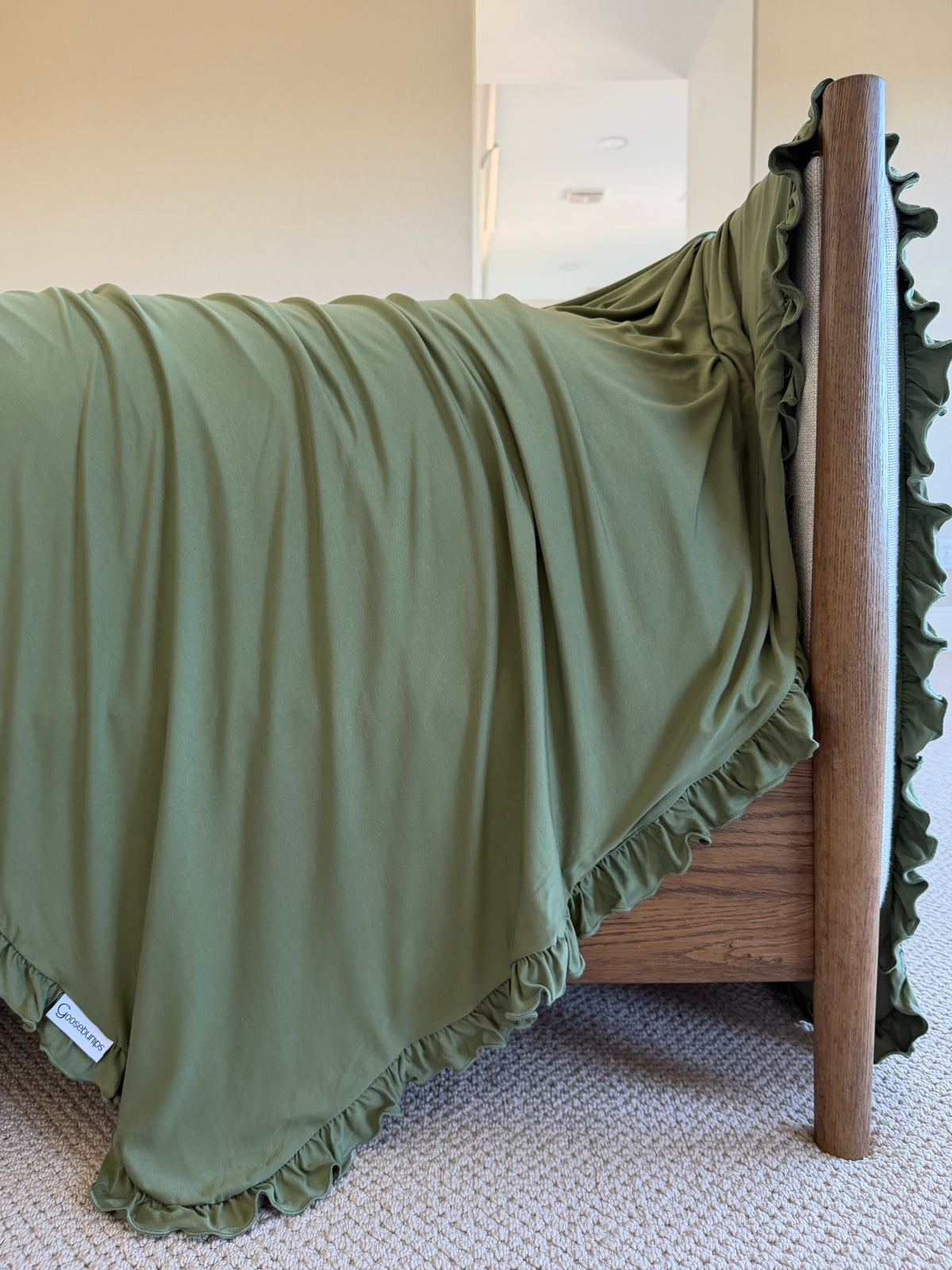 Winter pine / ruffle olive green bamboo blanket with a ruffled edge draped over a wooden bed frame.