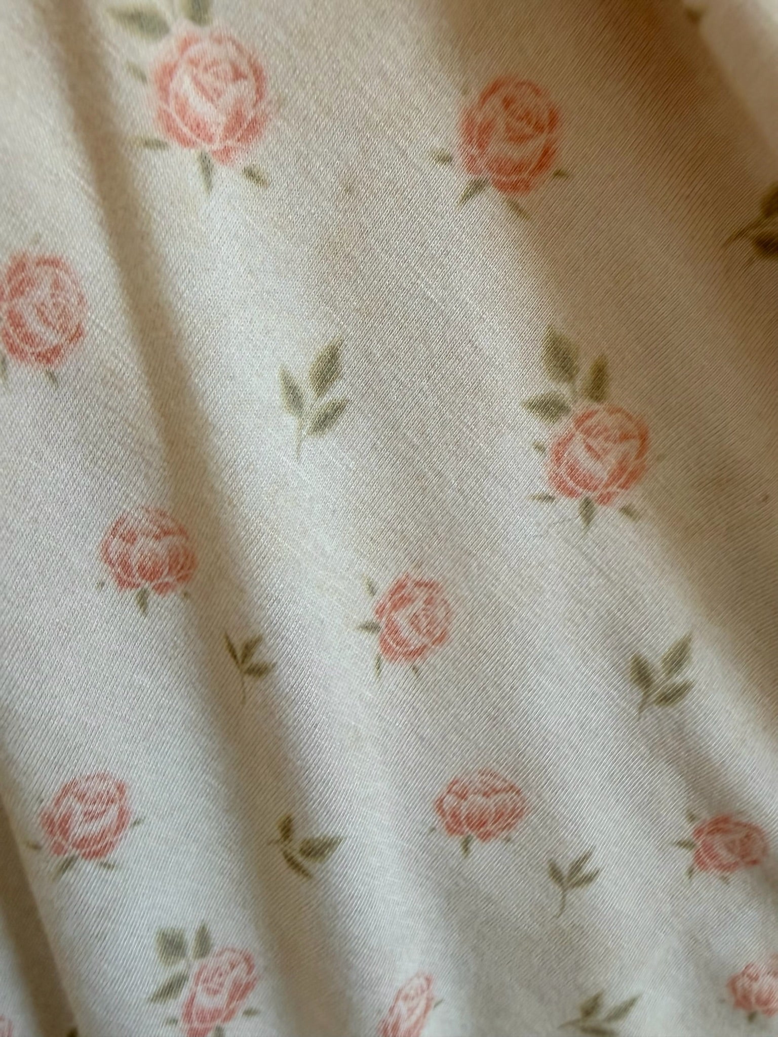 The "petal" is a cream-colored bamboo blanket featuring small pink roses and green leaves scattered evenly across its soft surface, creating gentle folds and soft shadows.