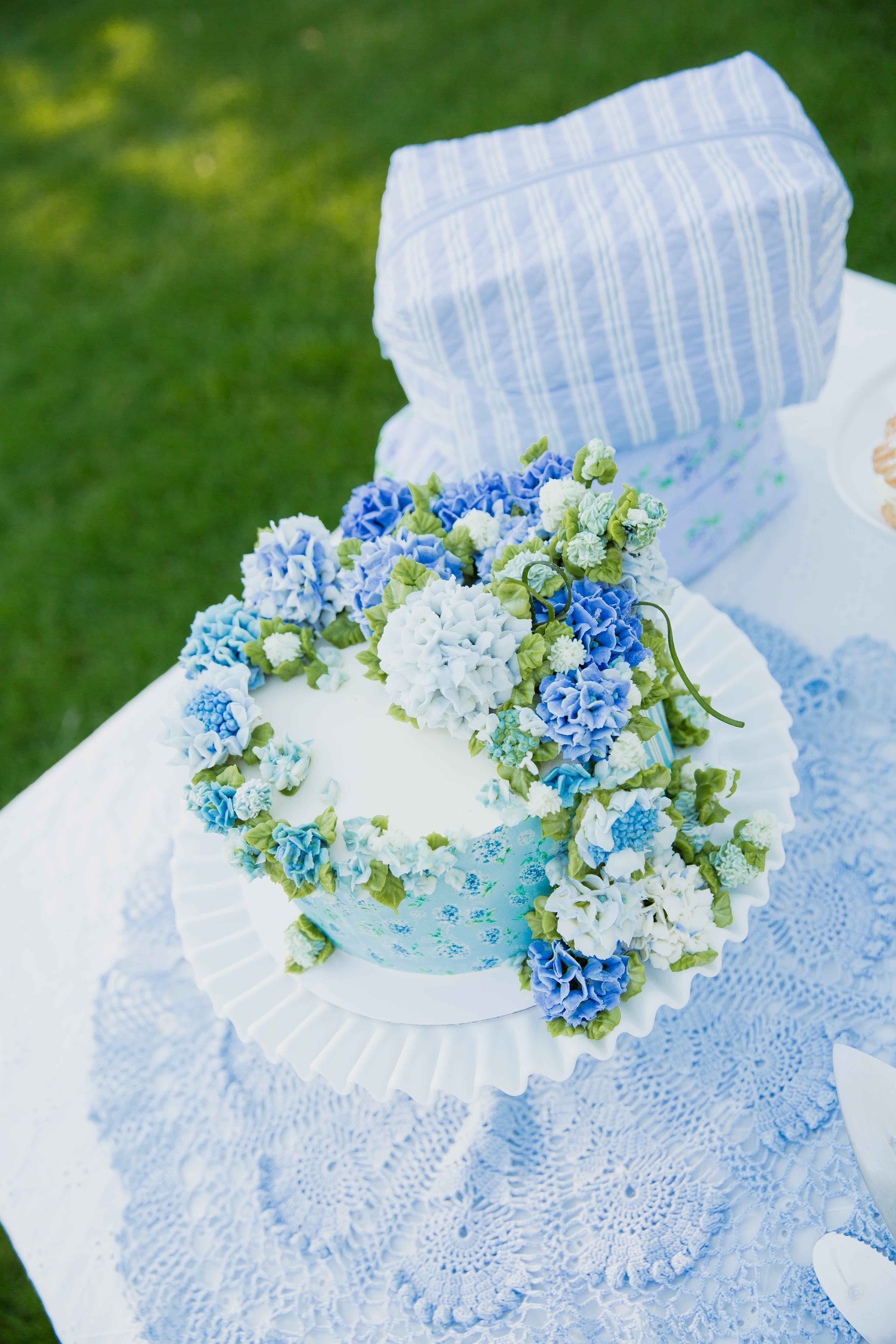 A haven / travel bag rests gracefully on a white stand atop a lace tablecloth, with grass in the background—making it a charming centerpiece for weekend getaways or any gathering where everyday essentials are celebrated.