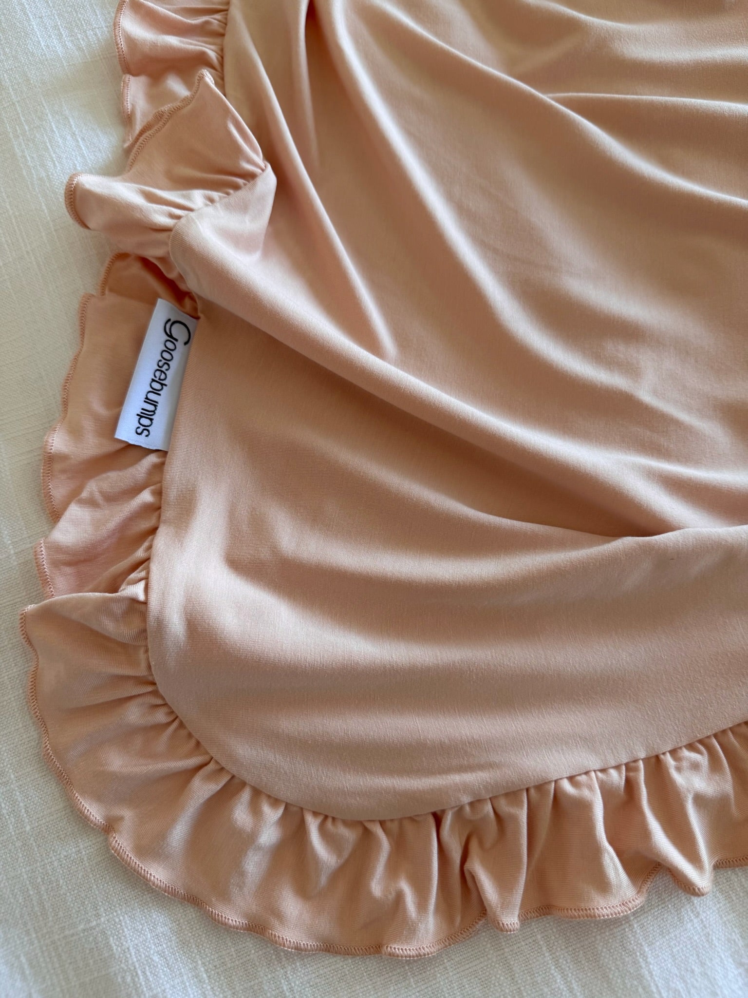 A close-up of a peach-colored whisp / ruffle bamboo viscose fabric with ruffle trim, draped over textured white, featuring a Cossésun Kids tag.