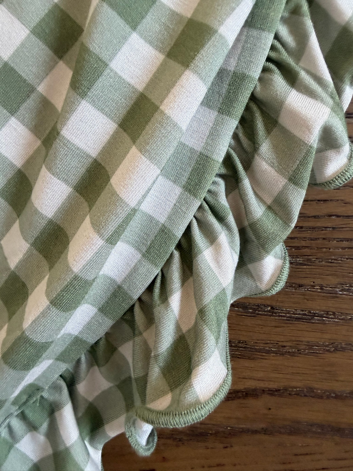 Evergreen lane / ruffle fabric in green and ivory gingham with a ruffled edge resting on a wooden surface.