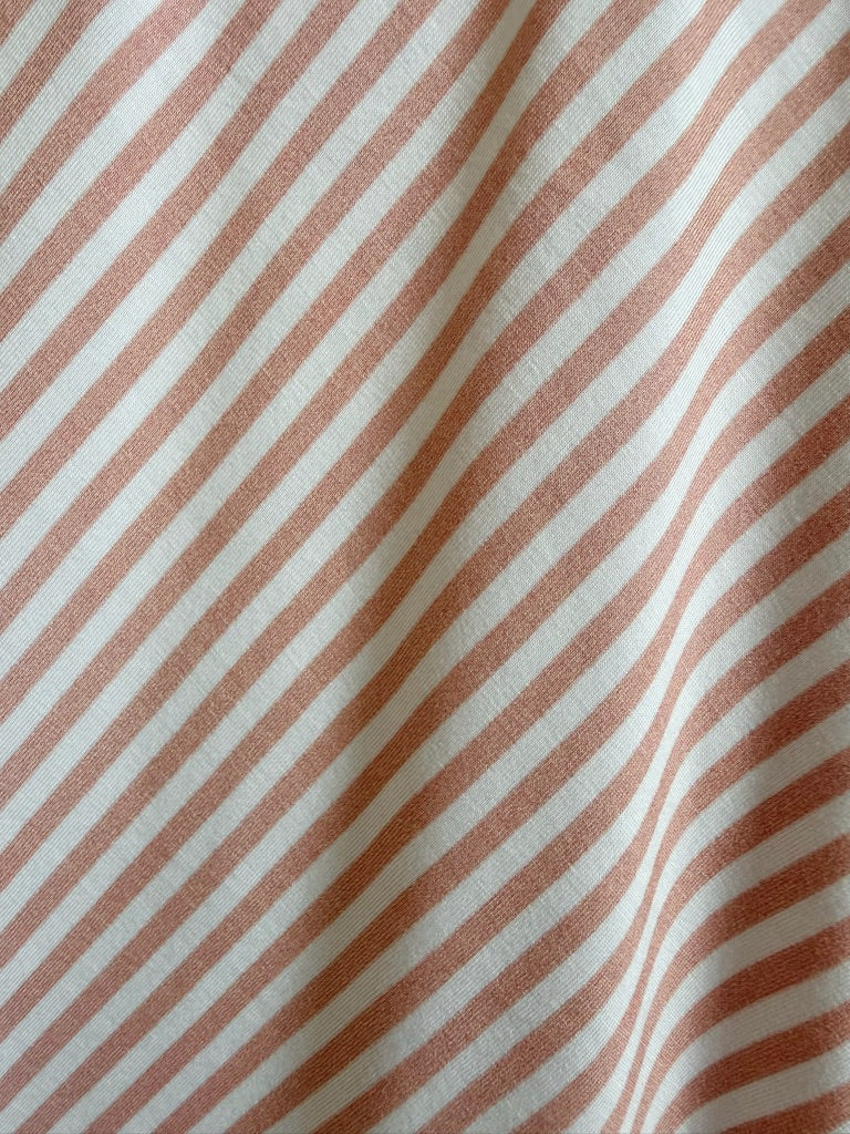 Close-up of the heritage / ruffle blanket in pink and ivory, featuring diagonal stripes. The luxurious blanket has a slightly wrinkled appearance, creating soft shadows and textured detail along its surface.
