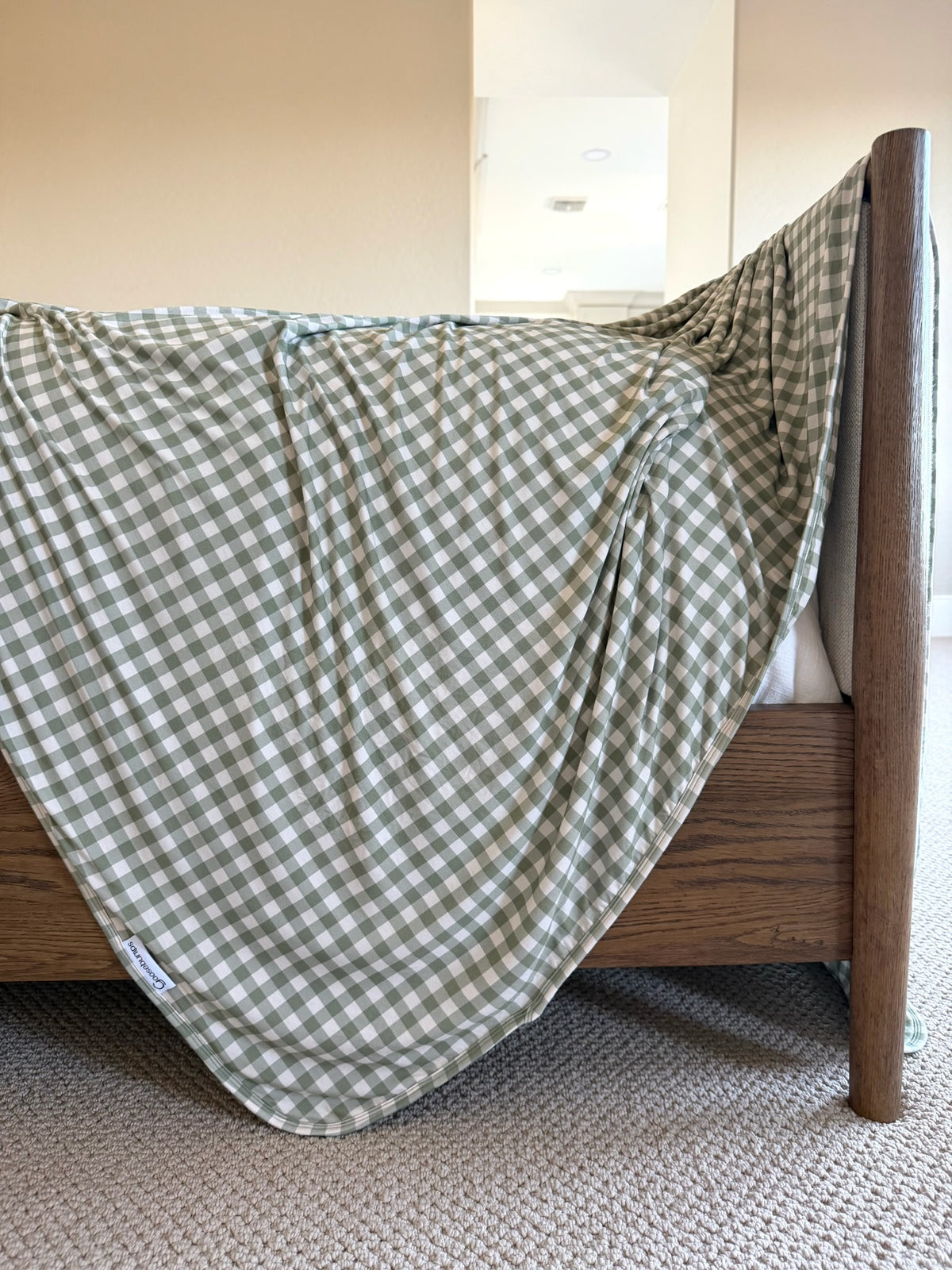 An evergreen lane bamboo blanket in a green and white gingham pattern draped over the foot of a wooden bed frame.