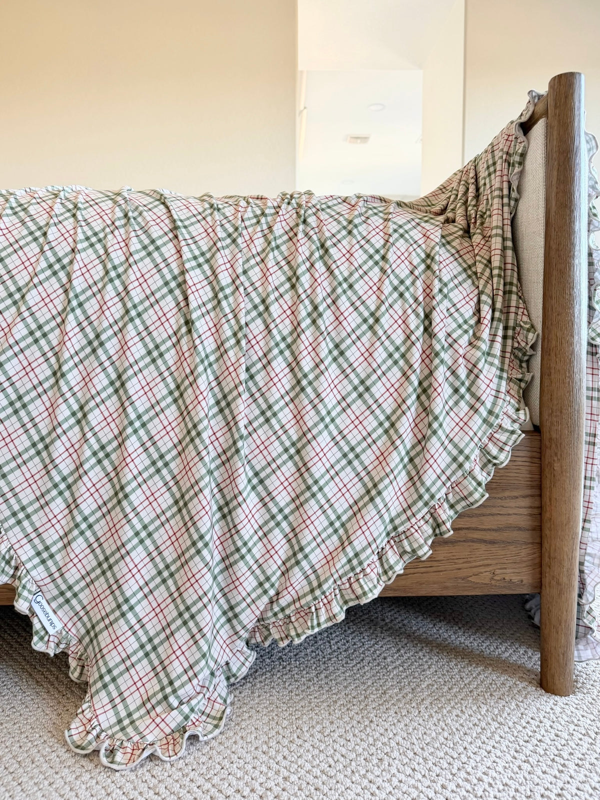 A luxurious homestead / ruffle plaid blanket with a ruffled edge draped over a wooden bed frame.