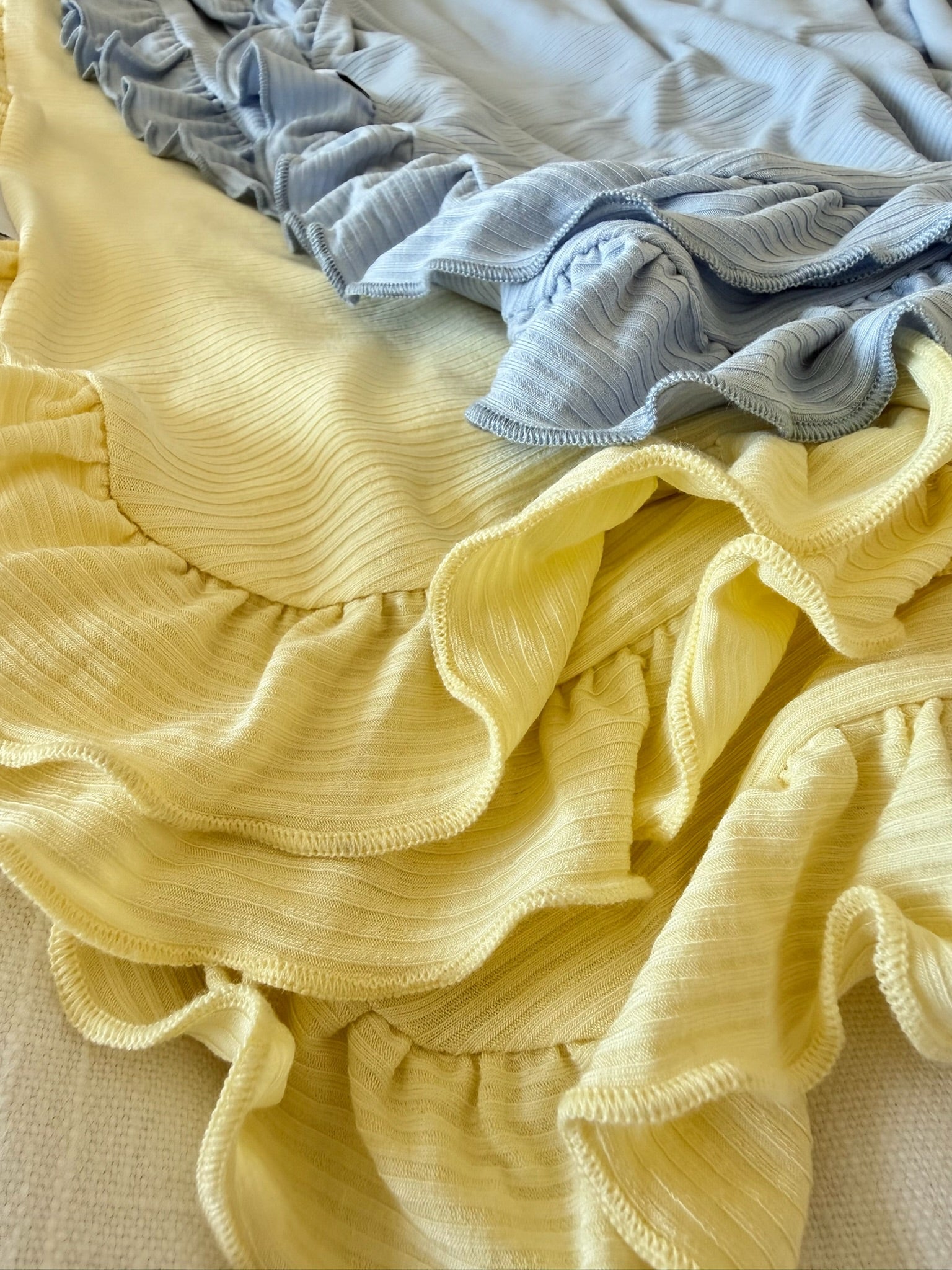 Close-up of the cove ribbed ruffle blanket in pastel yellow and light blue, layered to highlight its soft texture and elegant waves.