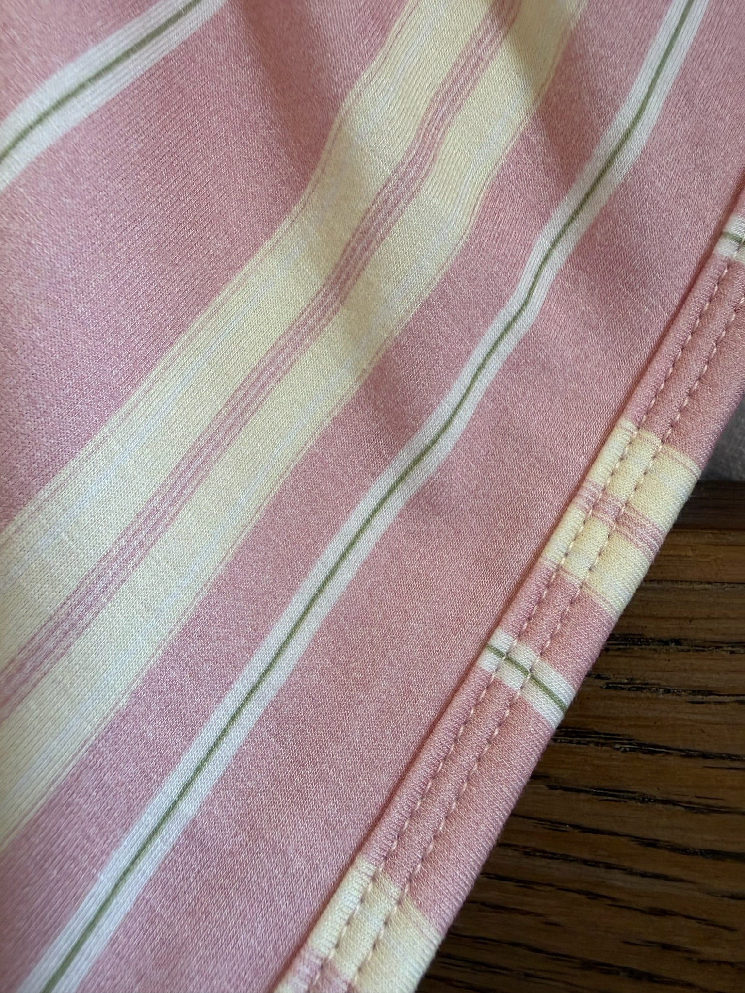 Close-up of Sherbet, a pink bamboo blanket with white and pale yellow vertical stripes and neatly stitched hem, resting on a wooden surface.