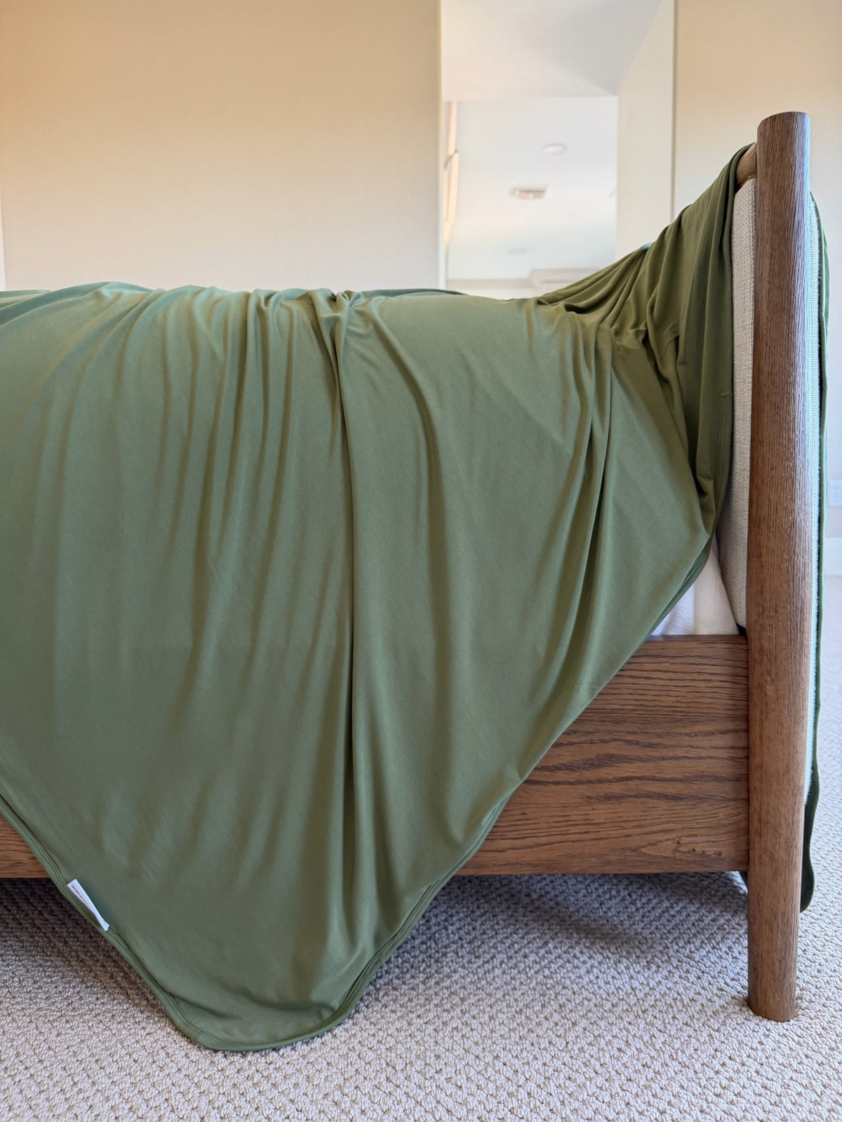 Luxurious olive green winter pine bamboo blanket draped over the footboard of a wooden bed frame.