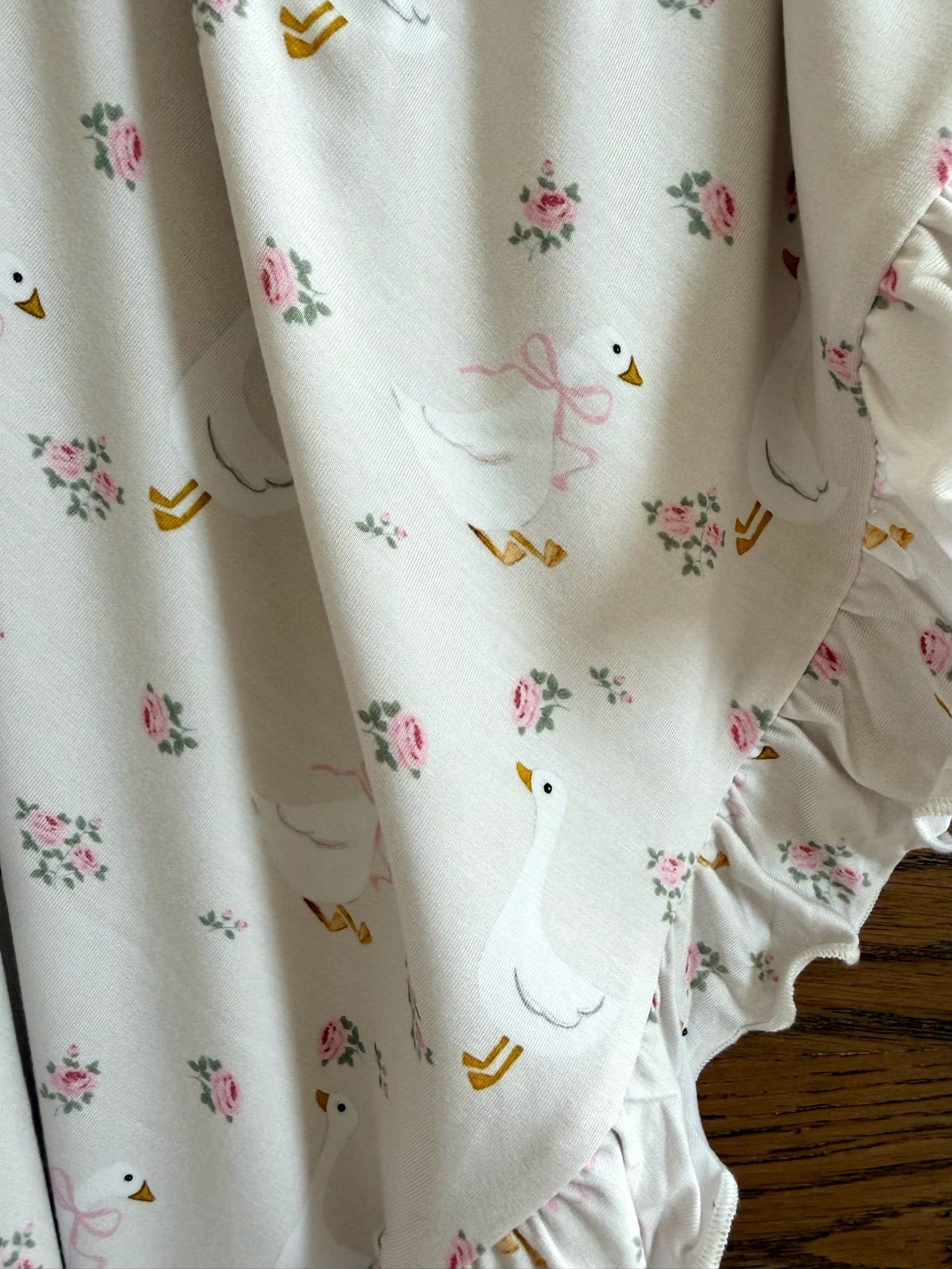 Close-up of the "mother goose / ruffle" blanket, featuring a floral print with white geese in pink bows and small pink roses—an adorable touch for any nursery.