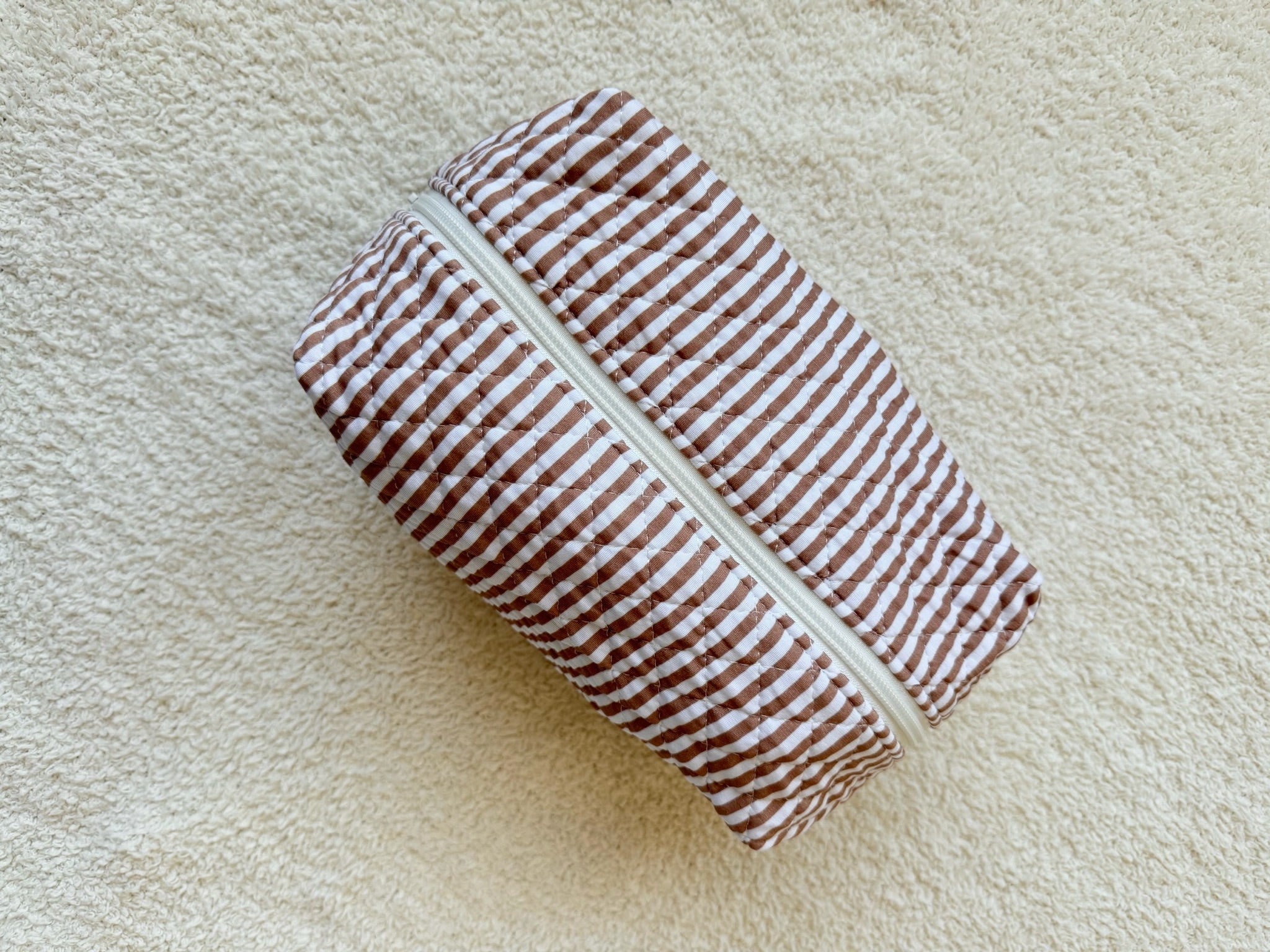 The drift / travel bag from the Lisa Wilson Goosebumps Collection features brown and white stripes and a white zipper, displayed on a beige textured surface.