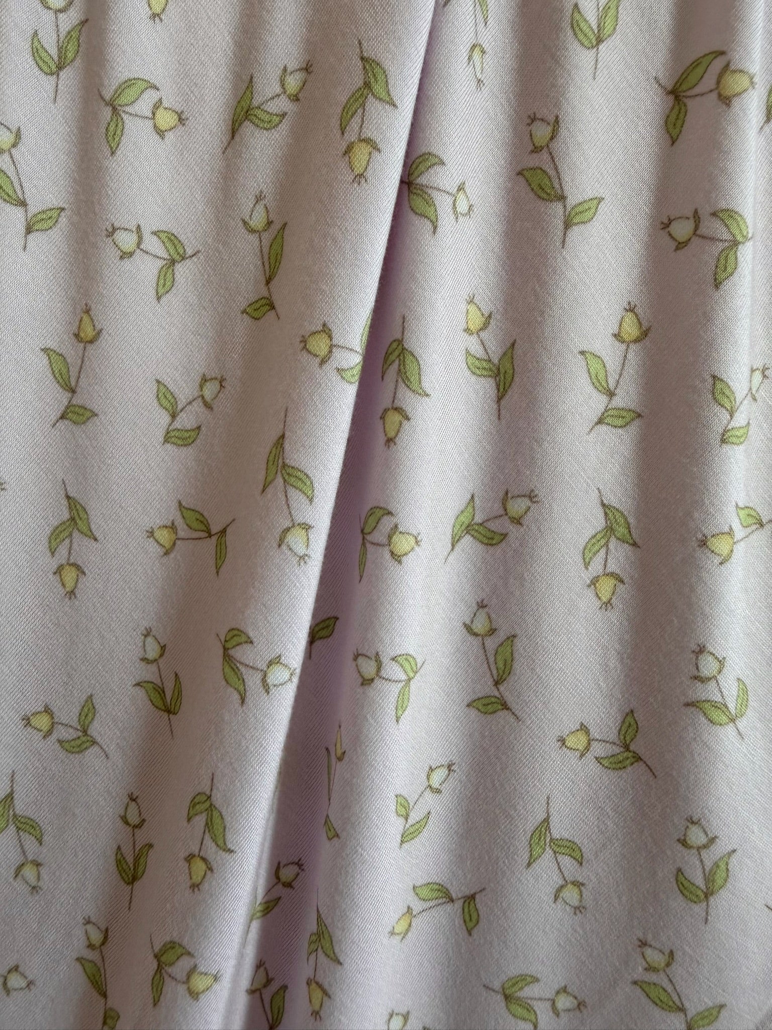 The rosebud blanket features light purple bamboo fabric with a repeated pattern of small green leafy stems and white flower buds, shown gently folded in the center—ideal for luxurious travel comfort.