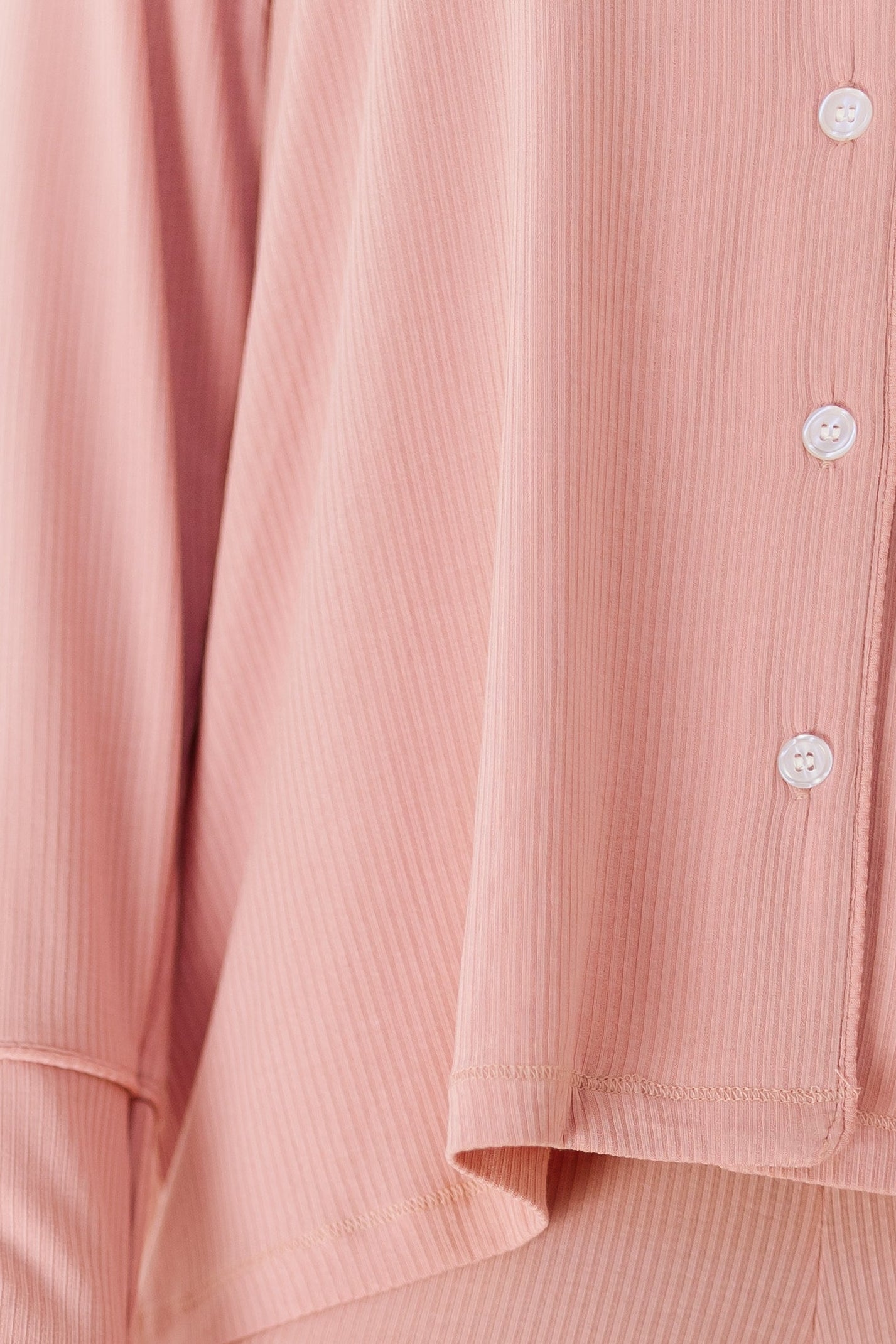 A person is shown from the torso down wearing our peony pajama set with long pants—relaxed fit, long sleeves, pink with white buttons—against a white background; only their torso, legs, and one hand are visible.