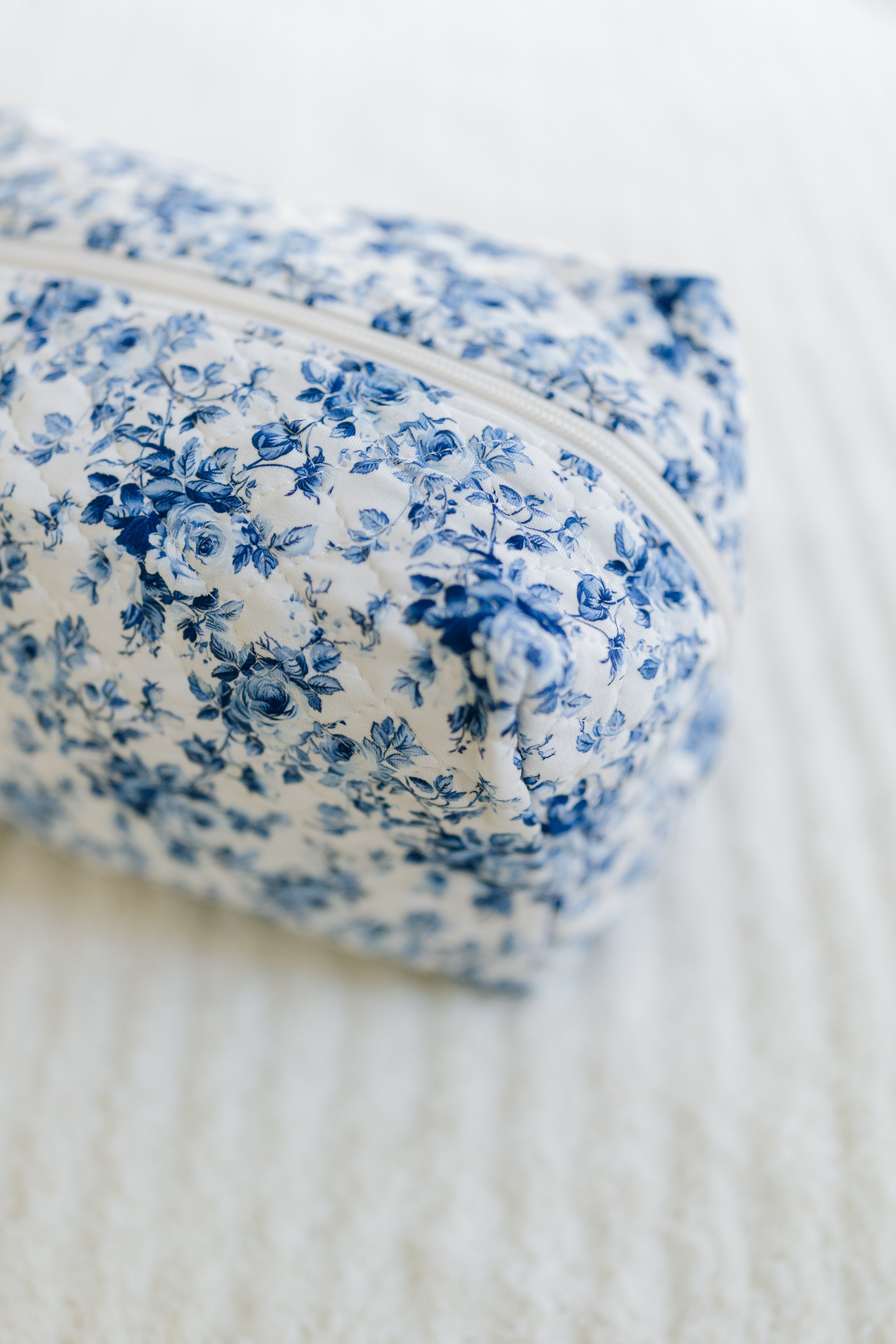 A close-up of the blue haven / travel bag—a rectangular white fabric pouch with a blue floral pattern and white zipper, ideal for storing your favorite travel accessories.