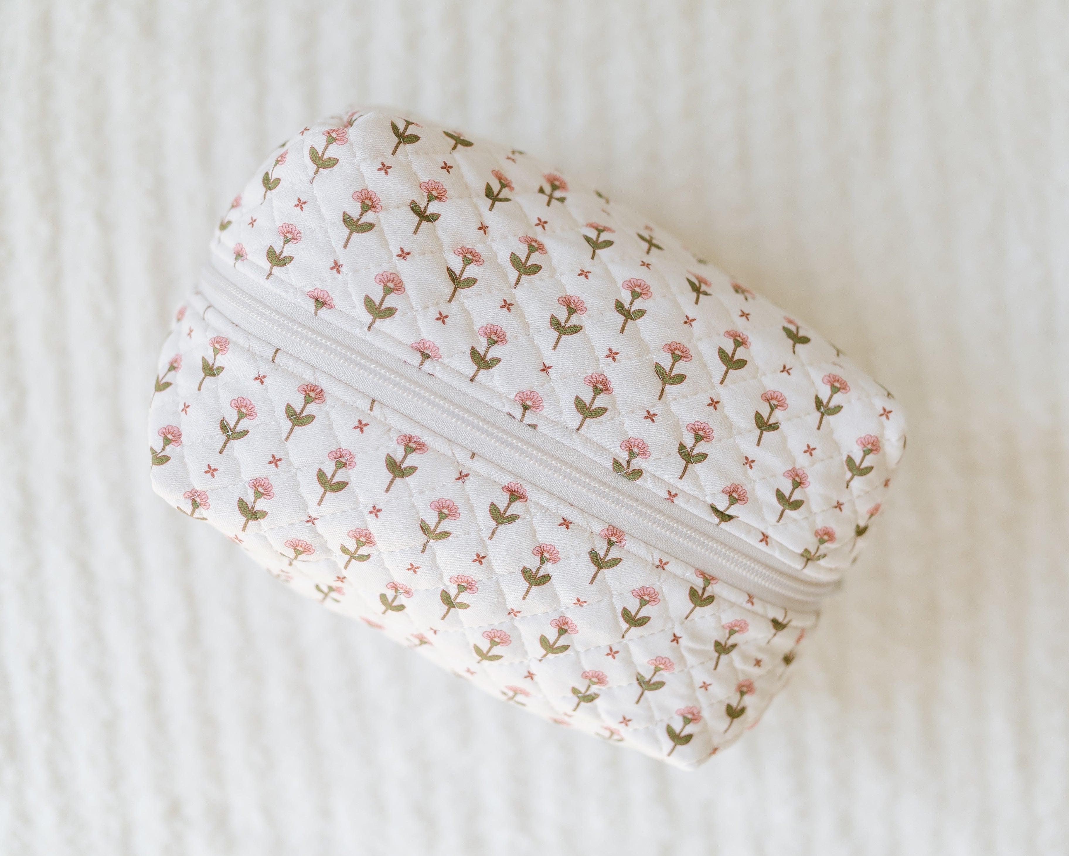 The tulip / travel bag is a small rectangular zipper pouch with a white background and delicate pink and green tulip flowers, shown on a textured white surface.