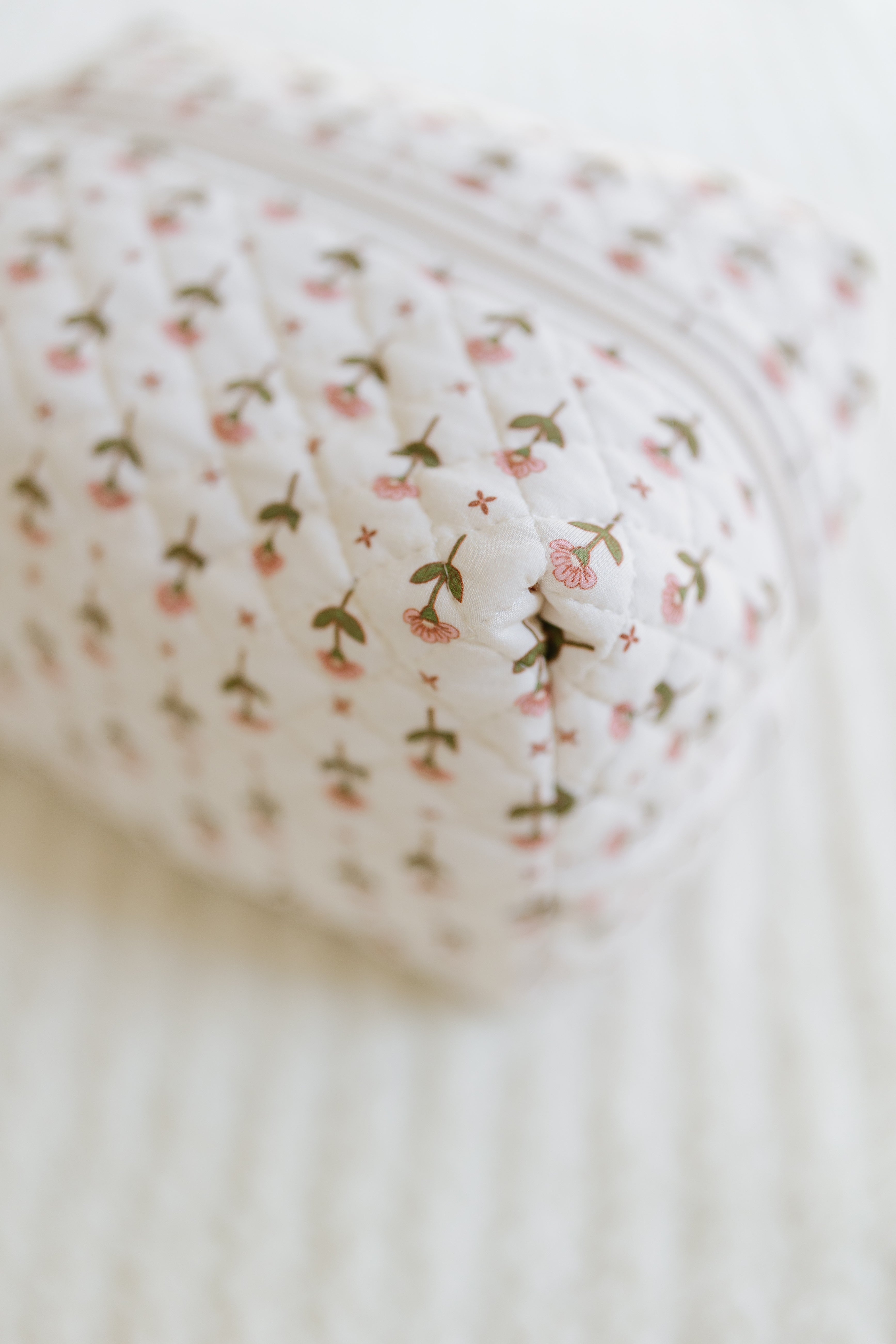 The tulip/travel bag is a quilted pouch with a zipper, decorated with small pink flowers and green stems, shown resting on a light textured surface.