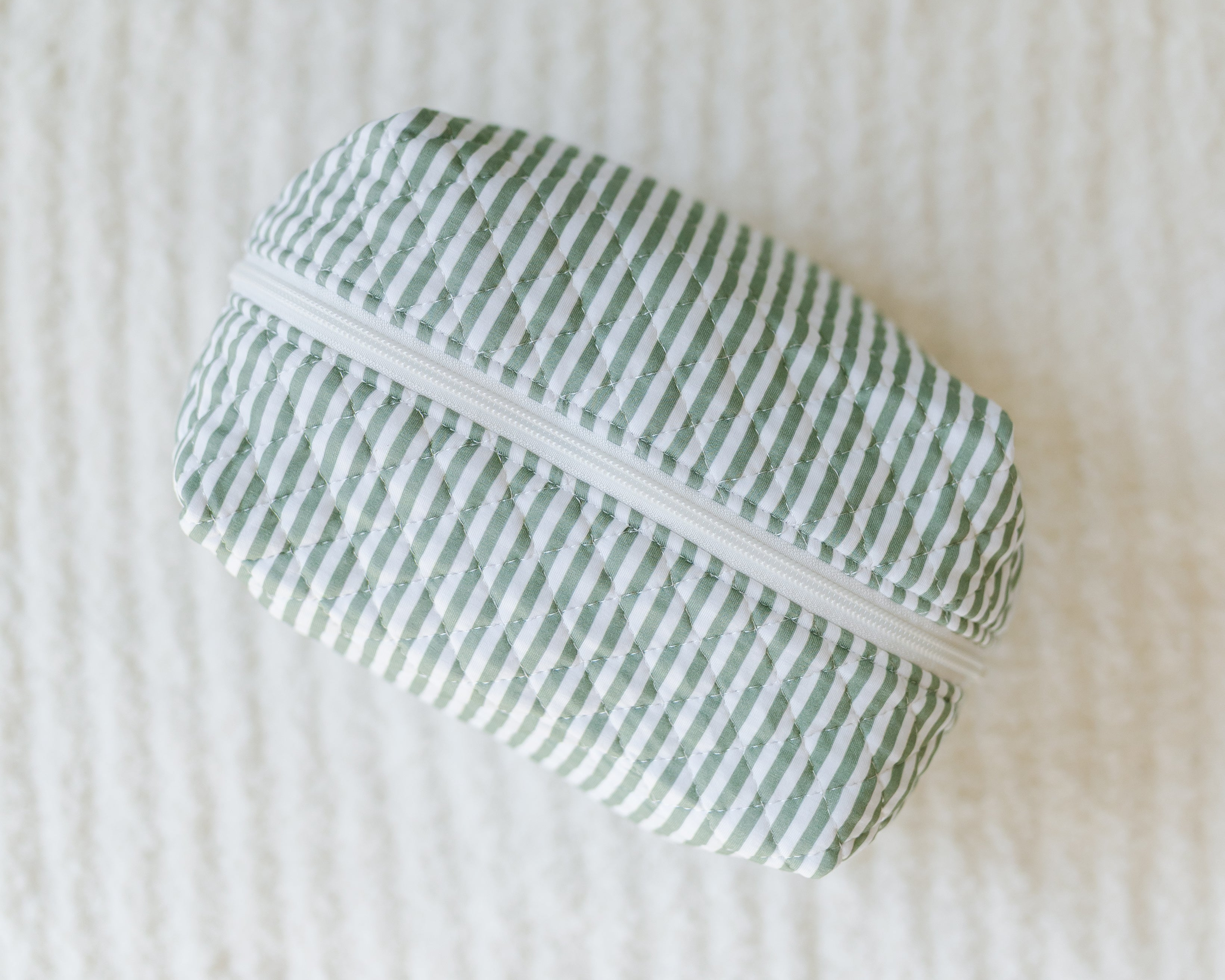 A tree house travel bag with green and white vertical stripes rests on a textured white surface, ideal for keeping your travel essentials organized.