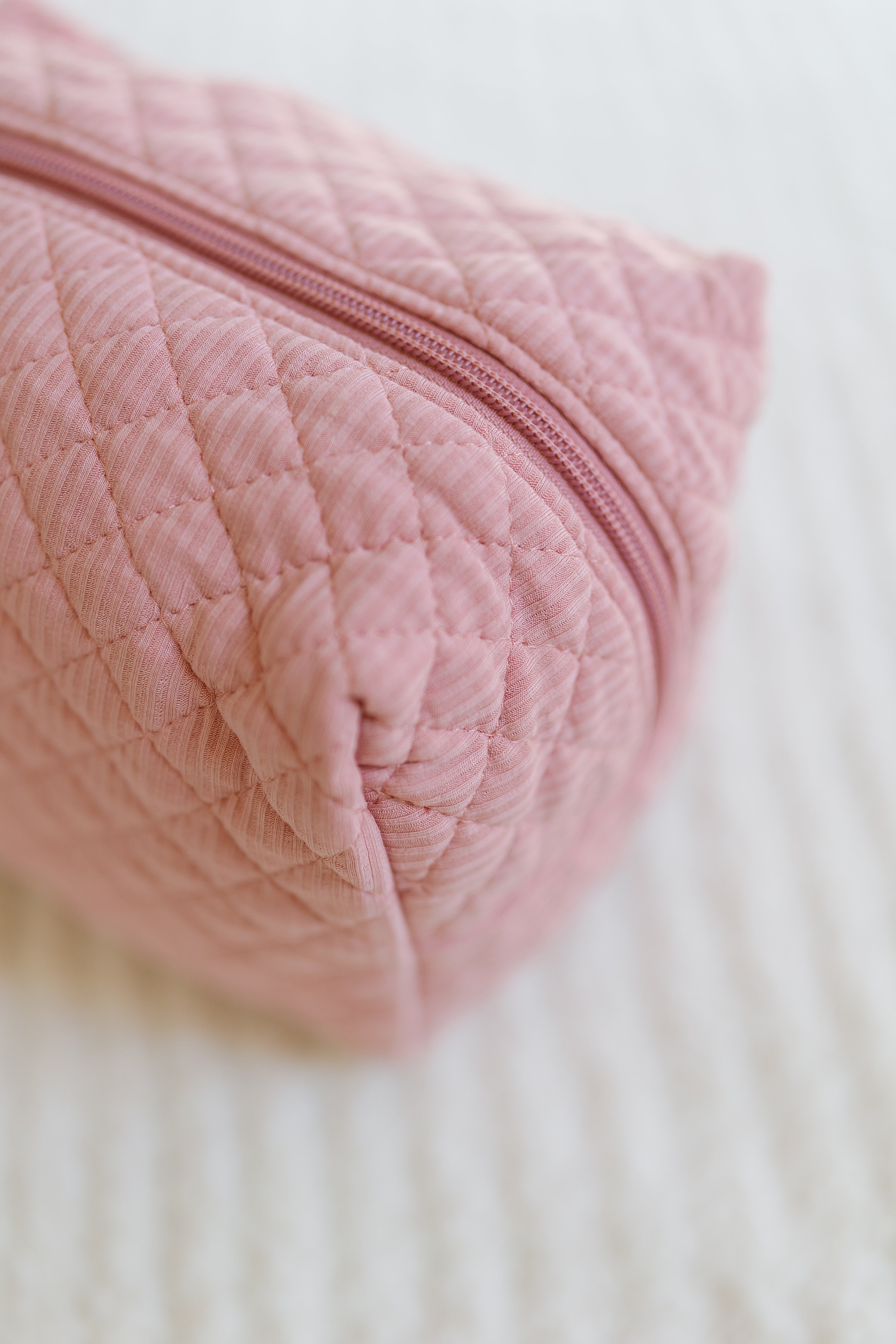 A close-up of the peony travel bag—a pink quilted pouch with a zipper—resting on a soft white surface, perfect for organizing essentials and one of the cutest travel accessories for trips.