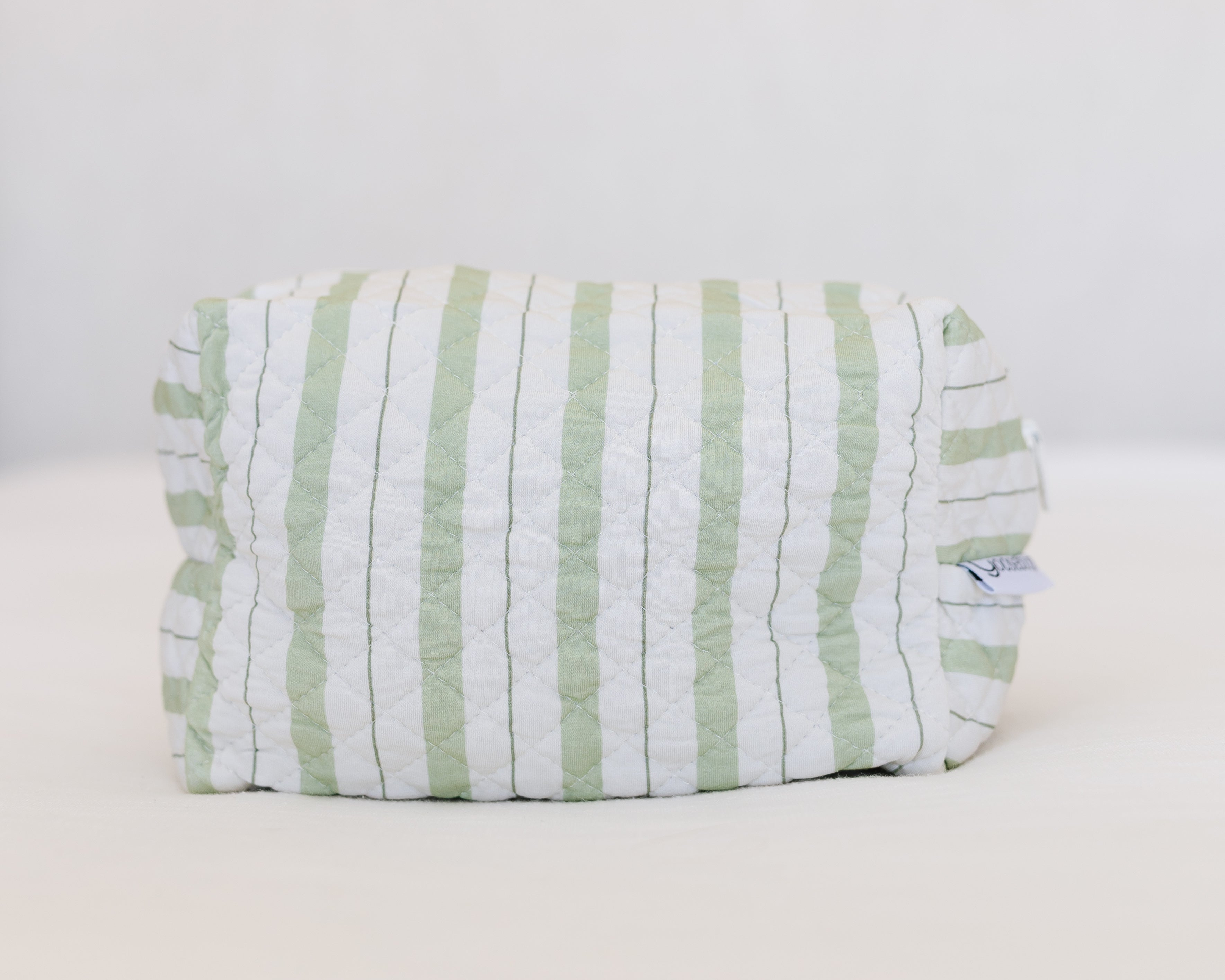 The gardener / travel bag is a rectangular quilted pouch with vertical light green and white stripes, made from soft bamboo viscose. A small tag appears on the right side as it rests on a plain white surface.