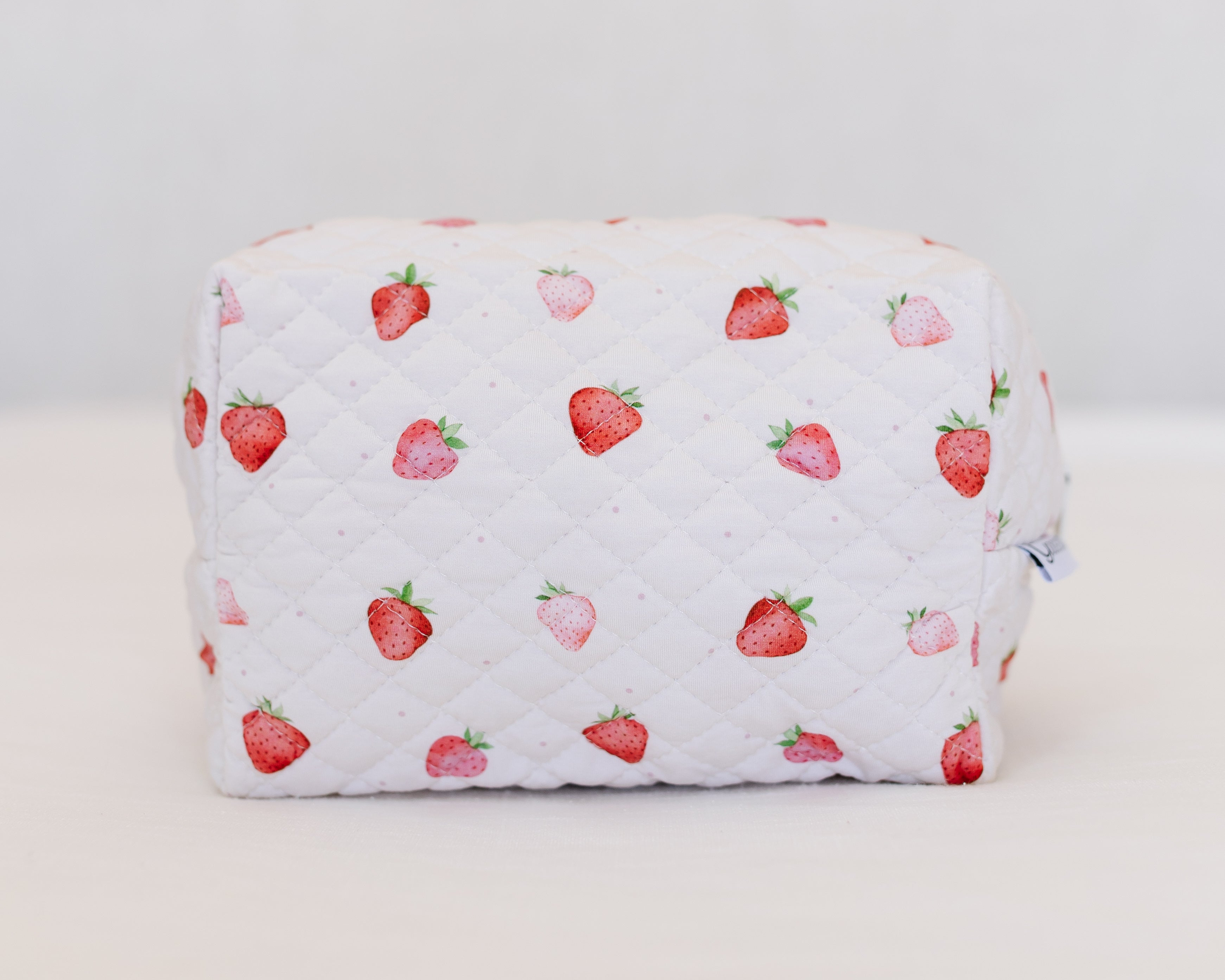 The strawberry shortcake / travel bag features a white quilted design with a red and pink strawberry print, displayed on a white surface against a light background.