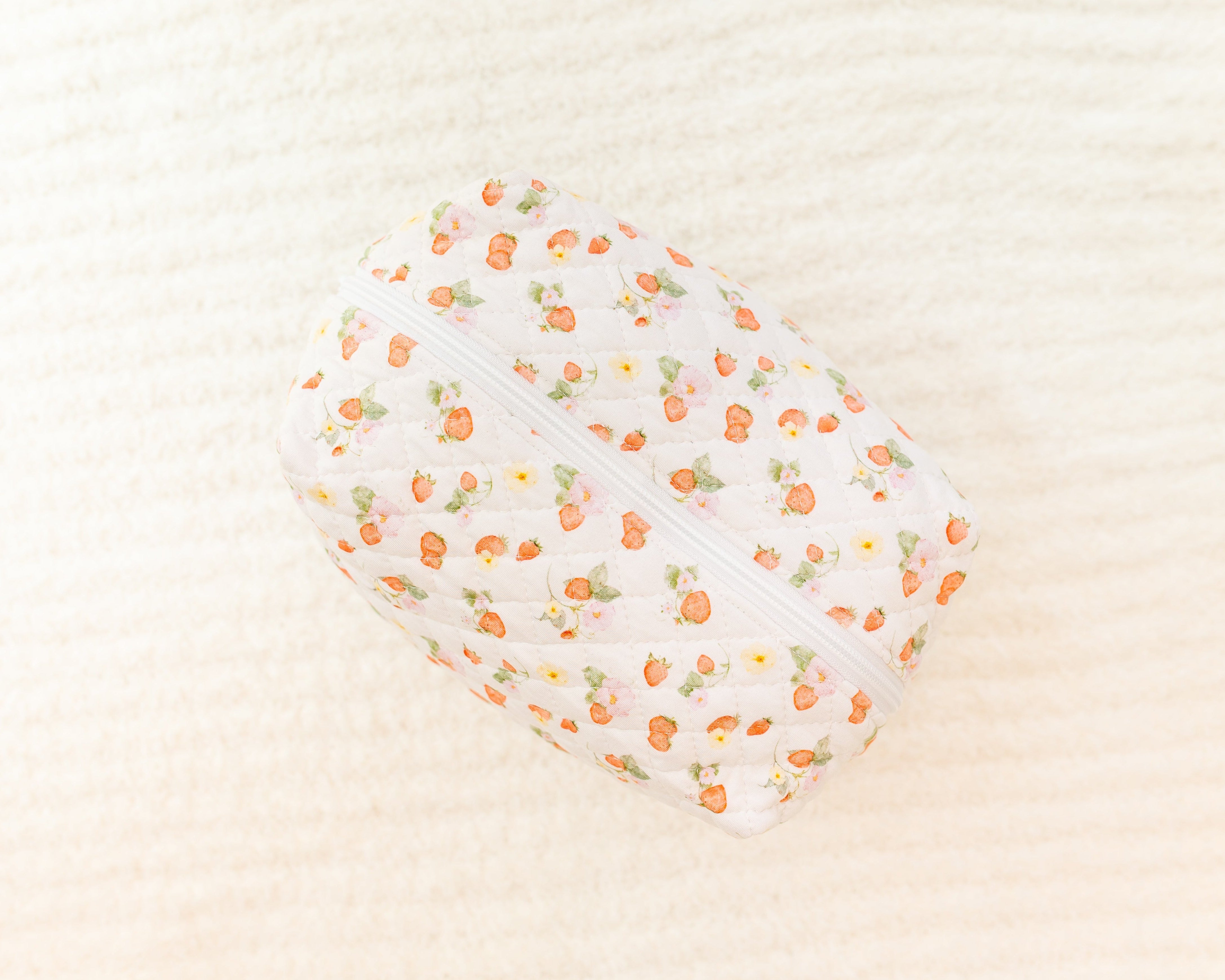 The freshly picked / travel bag is a quilted, zippered pouch featuring a small orange and green fruit pattern, ideal for travel, resting on a softly textured cream surface.