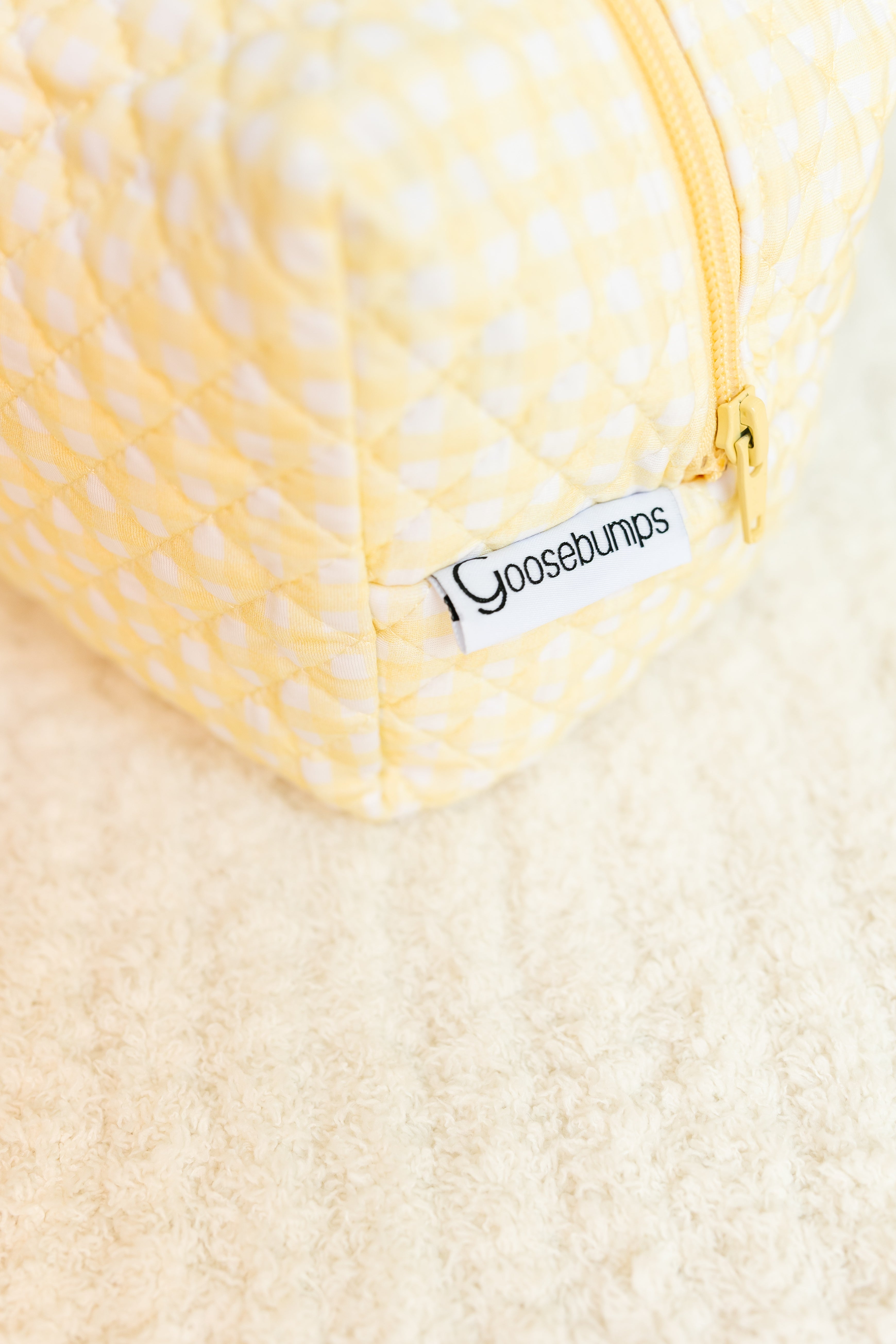 A close-up of the sunshine / travel bag, featuring a yellow-and-white checkered design with a yellow zipper and label, resting on a soft cream-colored surface—perfect for carrying your travel essentials in style.