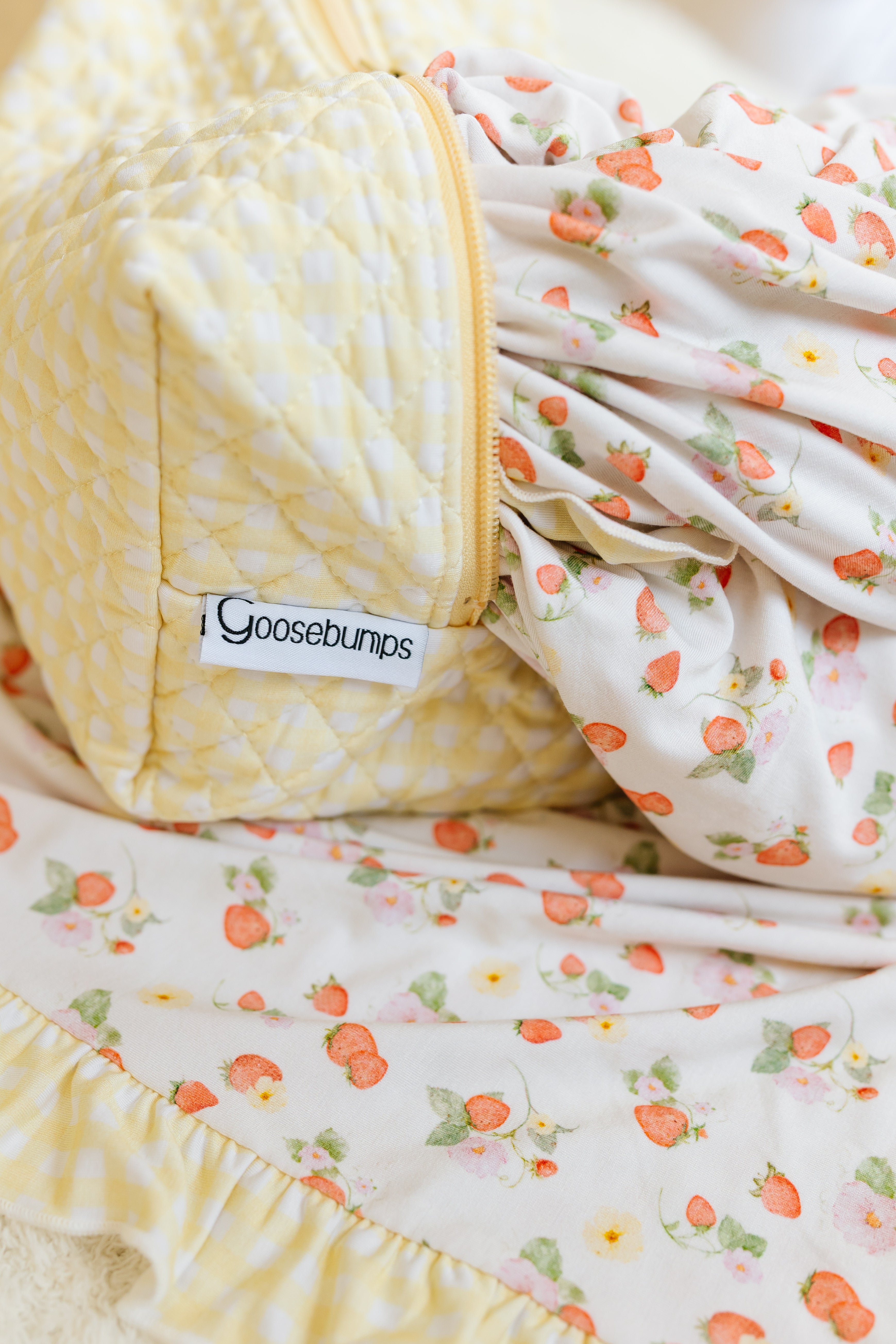 A close-up of the "freshly picked w/ sunshine ruffle"—a soft, quilted yellow and white fabric beside a cream bamboo blanket with strawberry prints and a Goosebumps label.