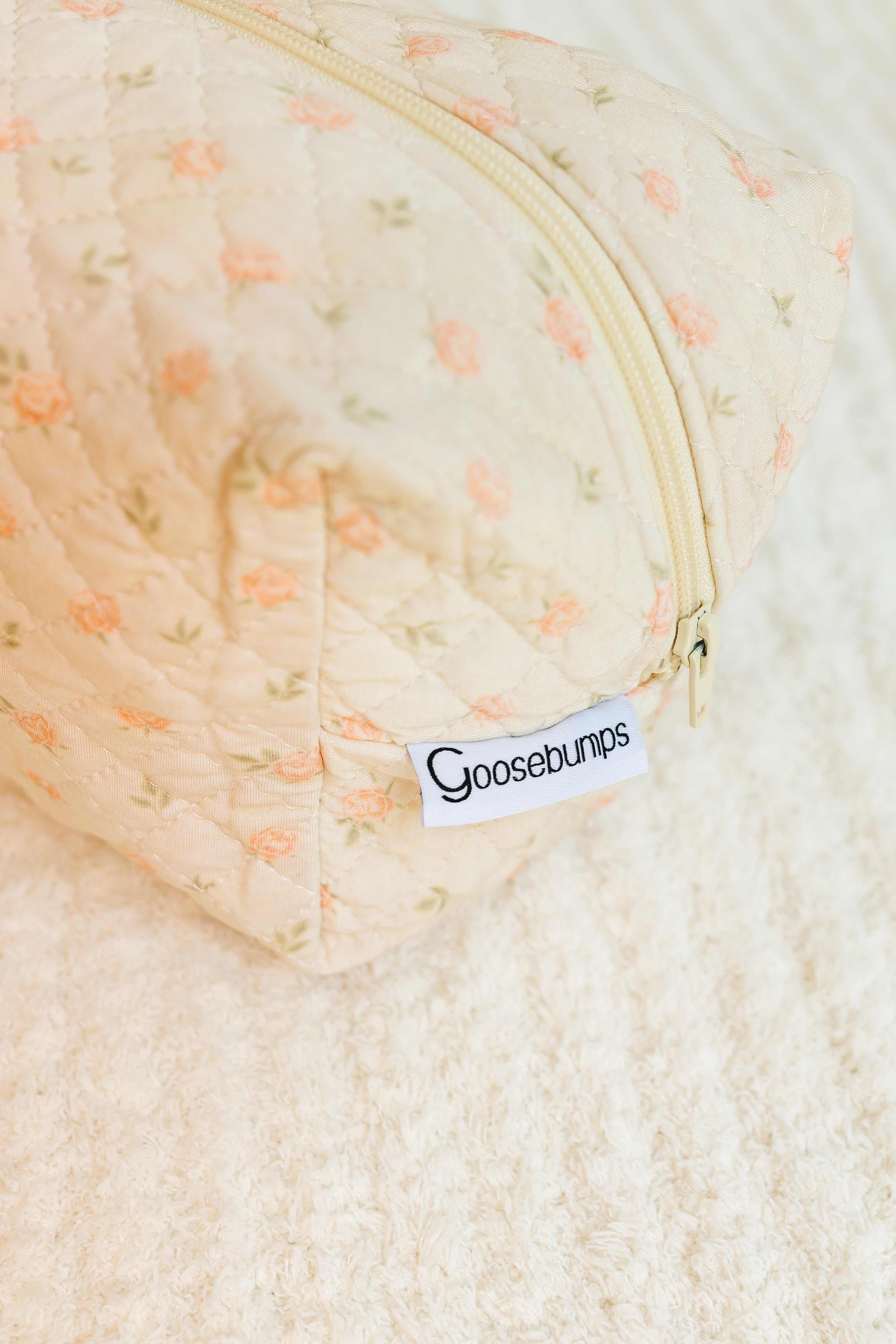 The petal / travel bag is a pastel quilted fabric bag with a floral pattern, beige zipper, and white Goosebumps tag, shown on a cream surface—ideal for carrying your travel accessories in style.