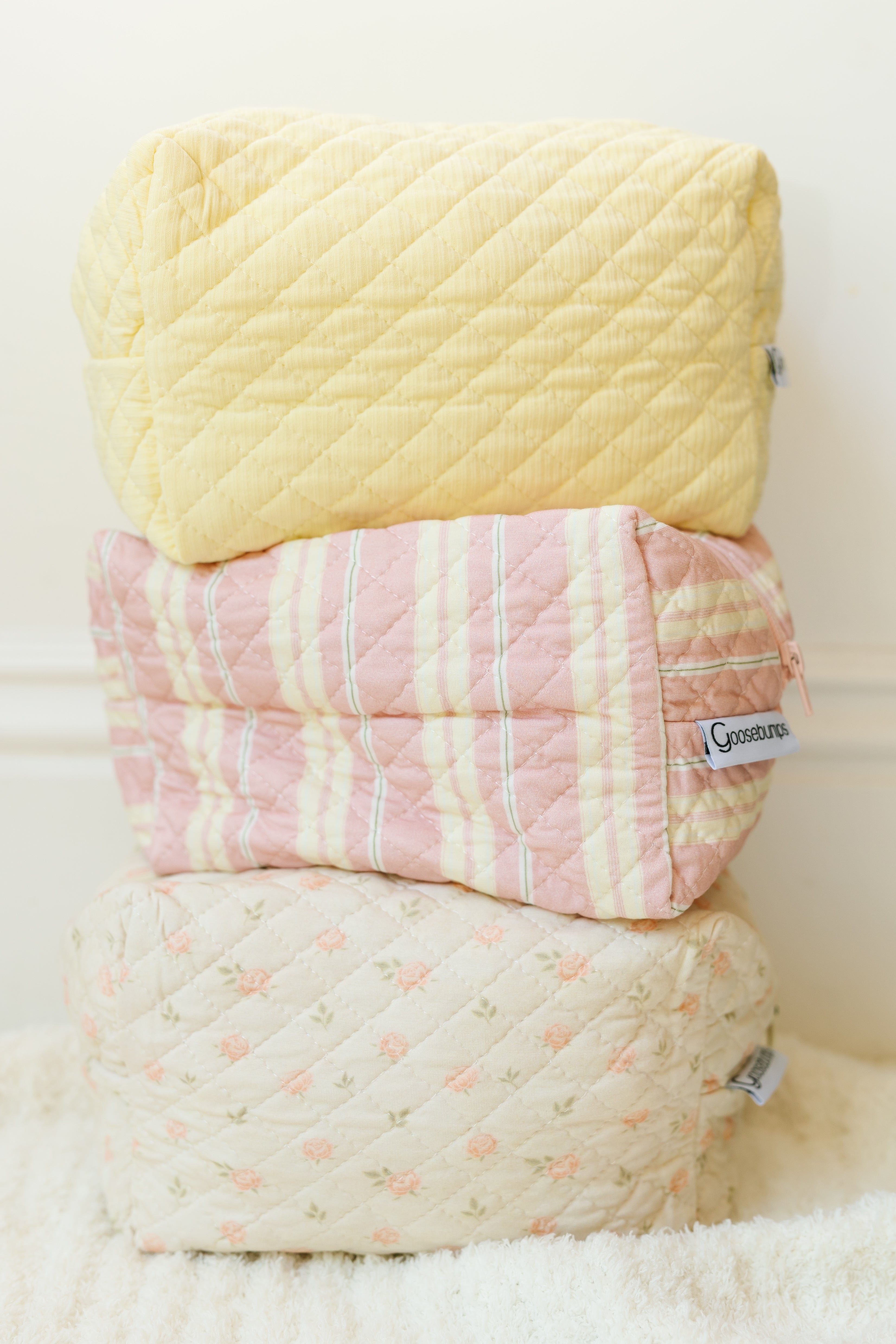 The petal / travel bag set includes three quilted pouches: a yellow top pouch, a pink and yellow striped middle pouch, and a bottom pouch with a cream base and small floral pattern—perfect for travel accessories.