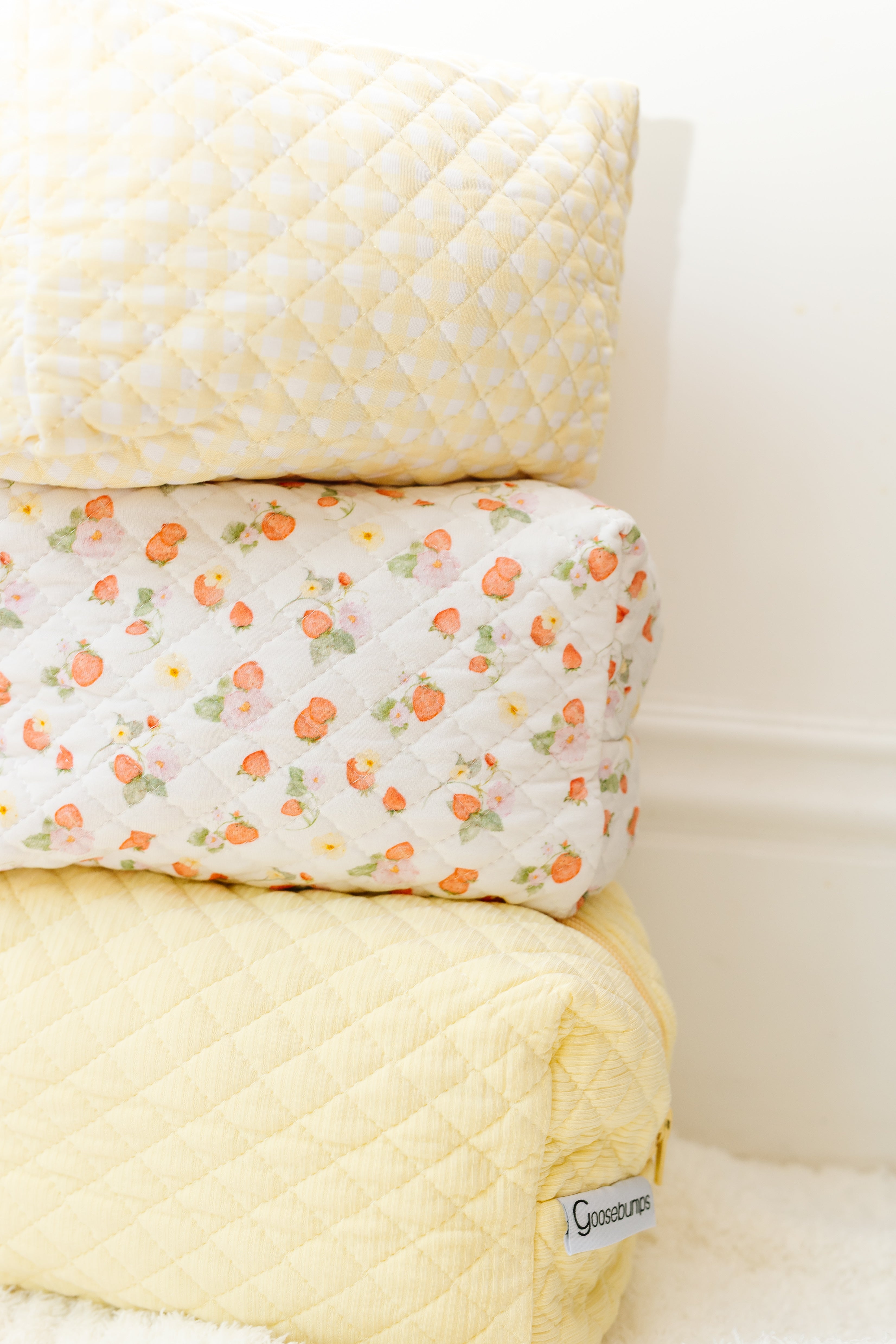 Three quilted cushions are stacked: the top and bottom are yellow with a diamond pattern, the middle is white with an orange floral design. A sunshine / travel bag tag is visible—great for organizing your travel accessories.