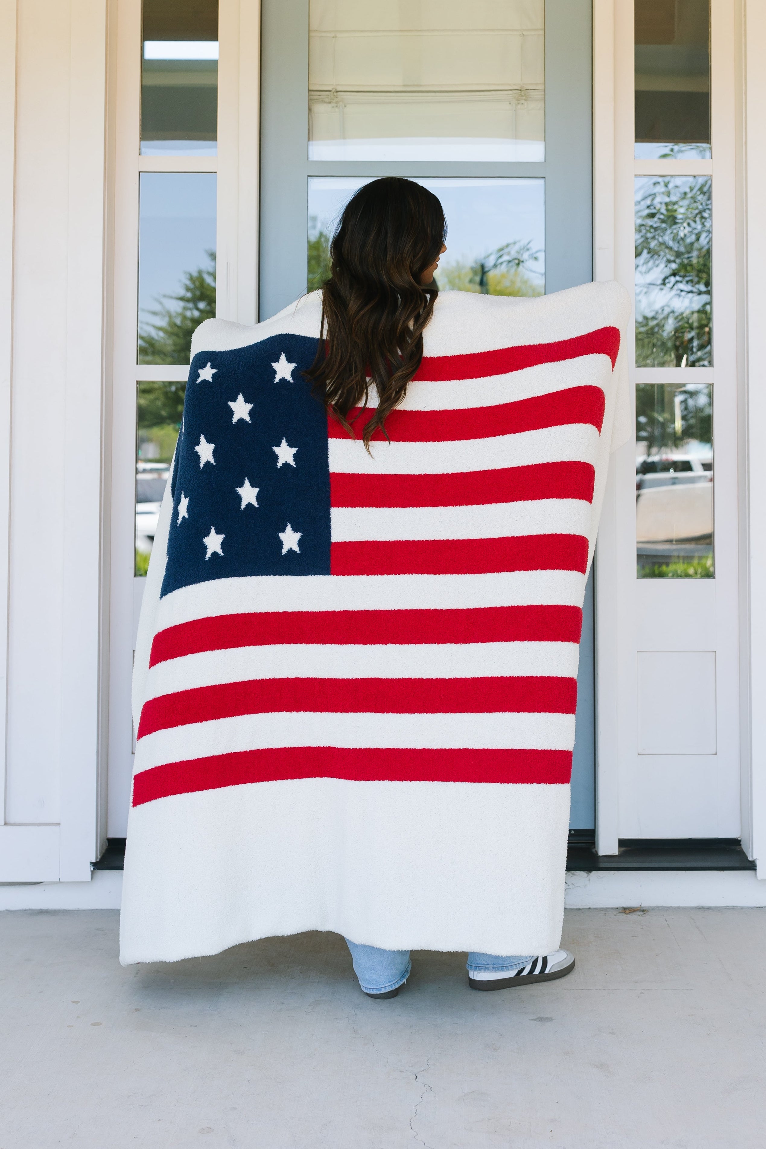 A person stands in front of a light blue door at house number 229, facing away and wrapped in the america / plush luxury lightweight blanket.