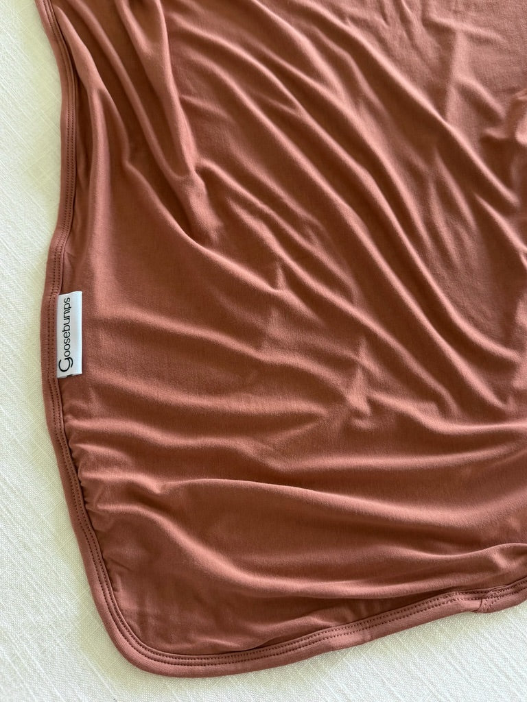 A light brown, slightly wrinkled serenity bamboo blanket with a white label that says SpearmintLOVE lies on a textured cream surface.