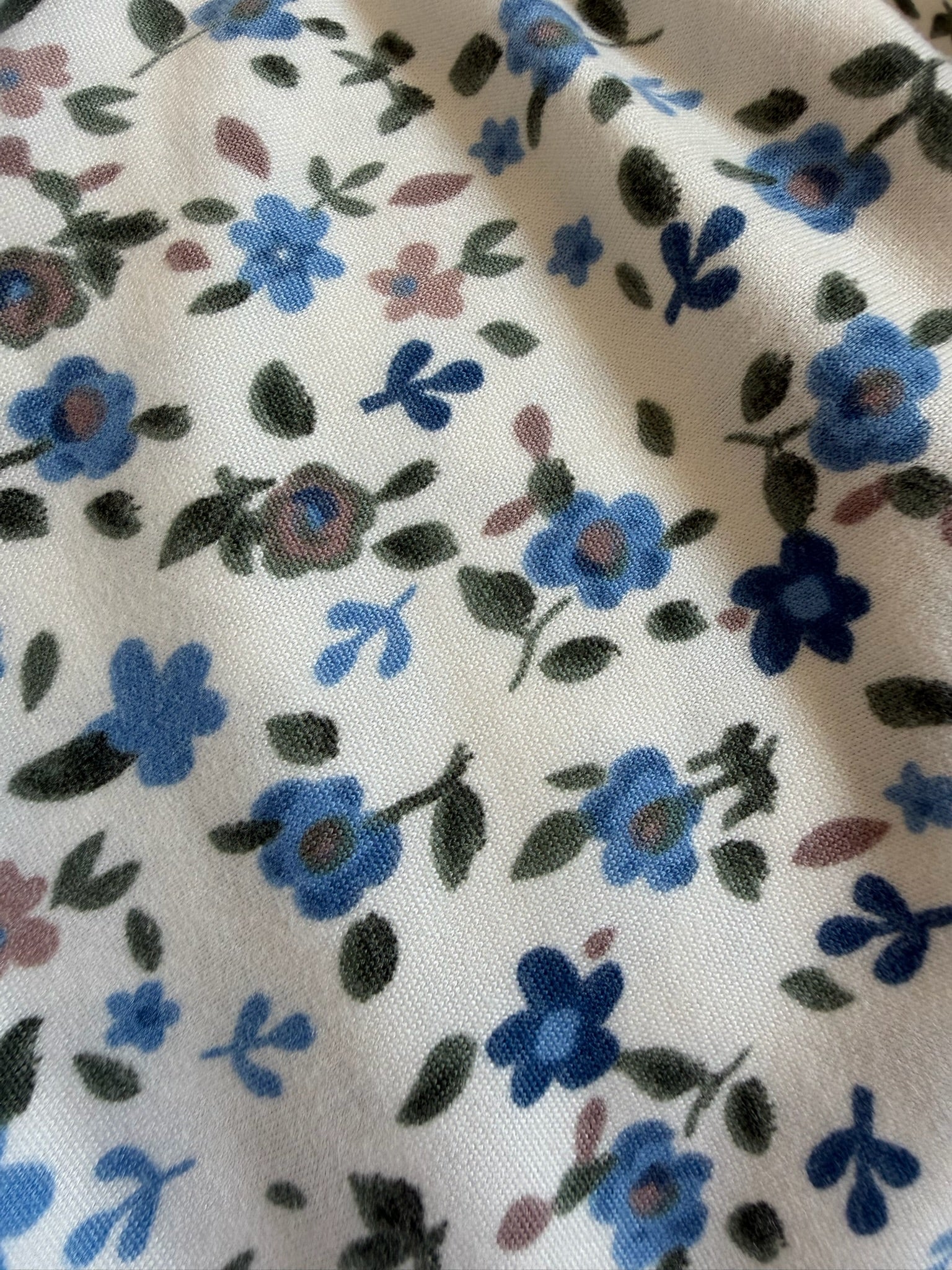 Choose Me features a white fabric printed with blue and purple flowers and green leaves. This extra soft blanket has a gently wrinkled, slightly textured material, making it perfect for cozy comfort at home or as a travel blanket on the go.
