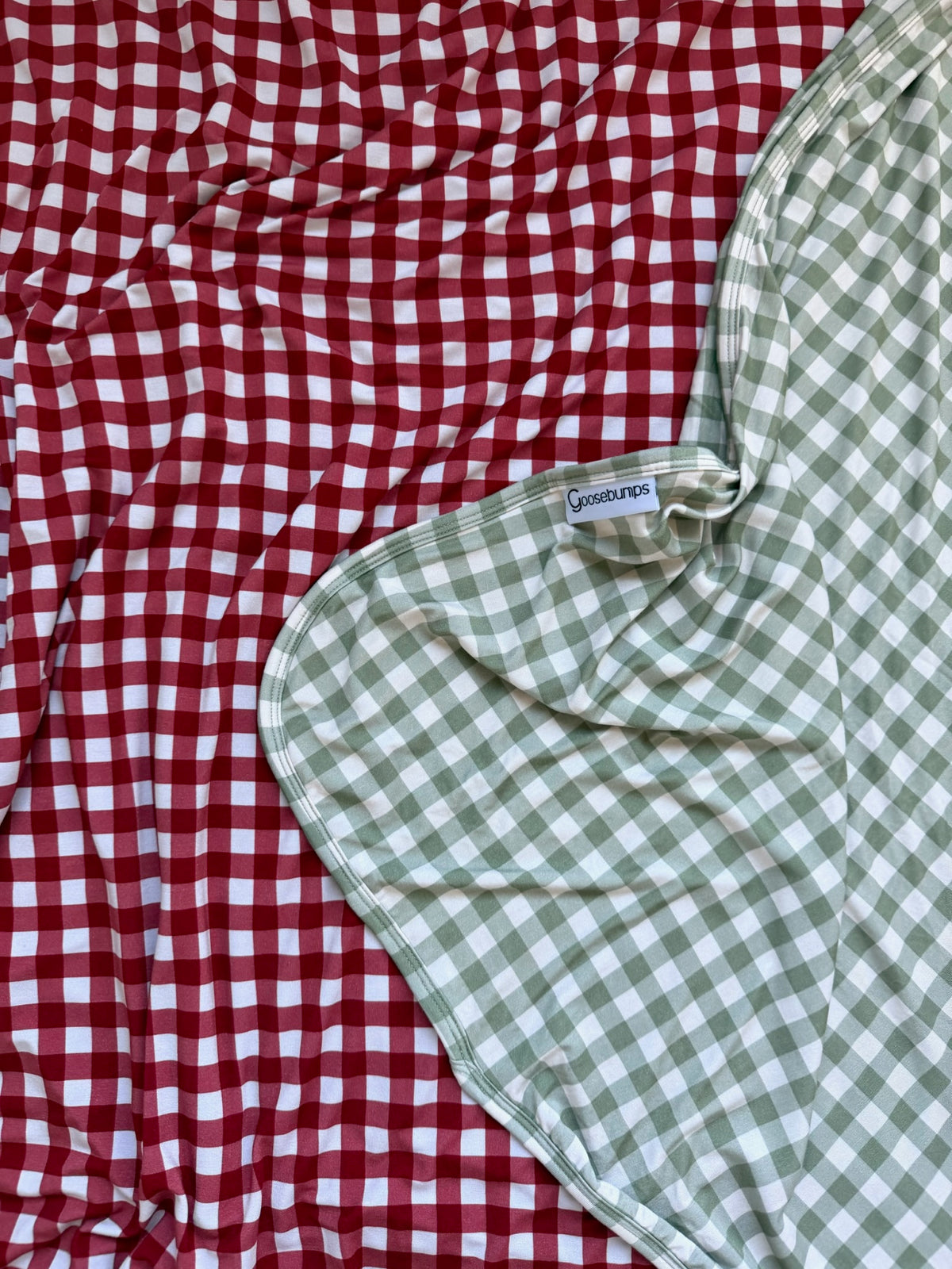 Evergreen lane bamboo blanket in sage green and white gingham layered over red and white gingham fabric.