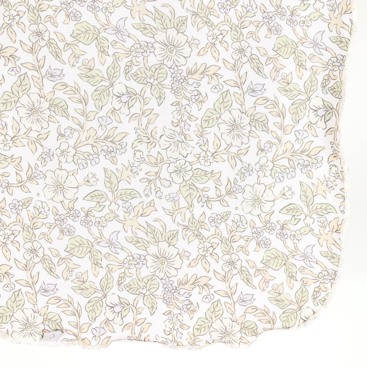 A close-up of the heirloom / swaddle, featuring bamboo fabric adorned with a delicate floral print in light green, beige, and pale yellow tones on a white background, with a scalloped edge visible at the bottom right.
