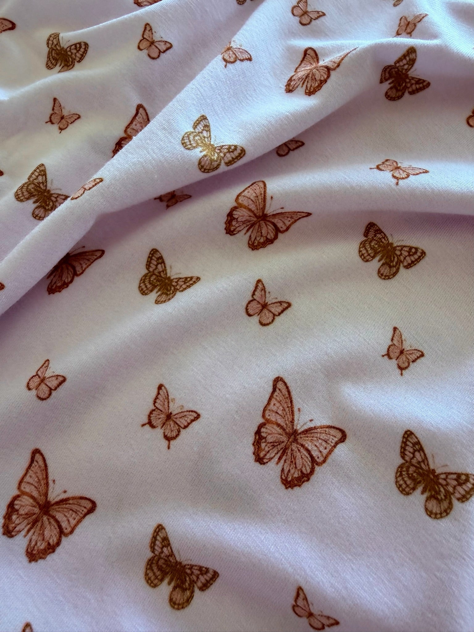 Close-up of “flutter / ruffle”: light bamboo viscose fabric featuring orange and brown butterflies. Gentle folds add texture and highlight its soft appearance—an ideal choice for an adult swaddle.