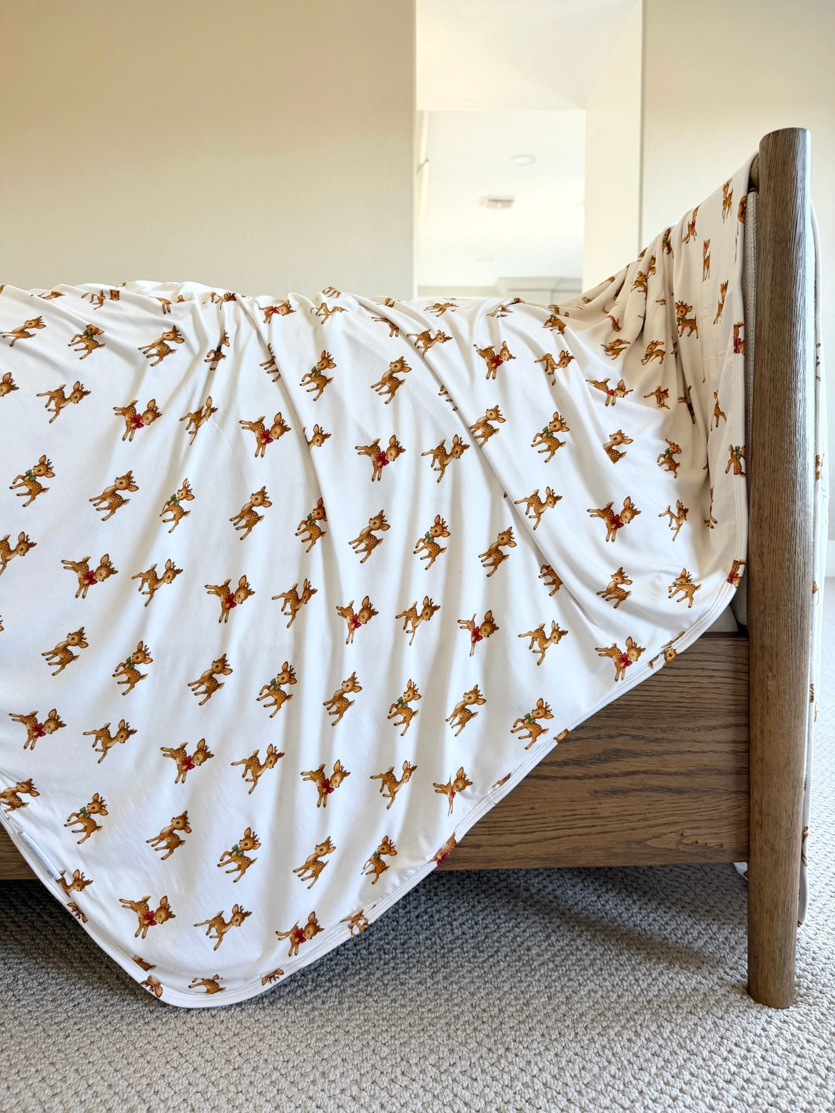 White bamboo blanket with a vintage reindeer pattern draped over the corner of a wooden bed frame.