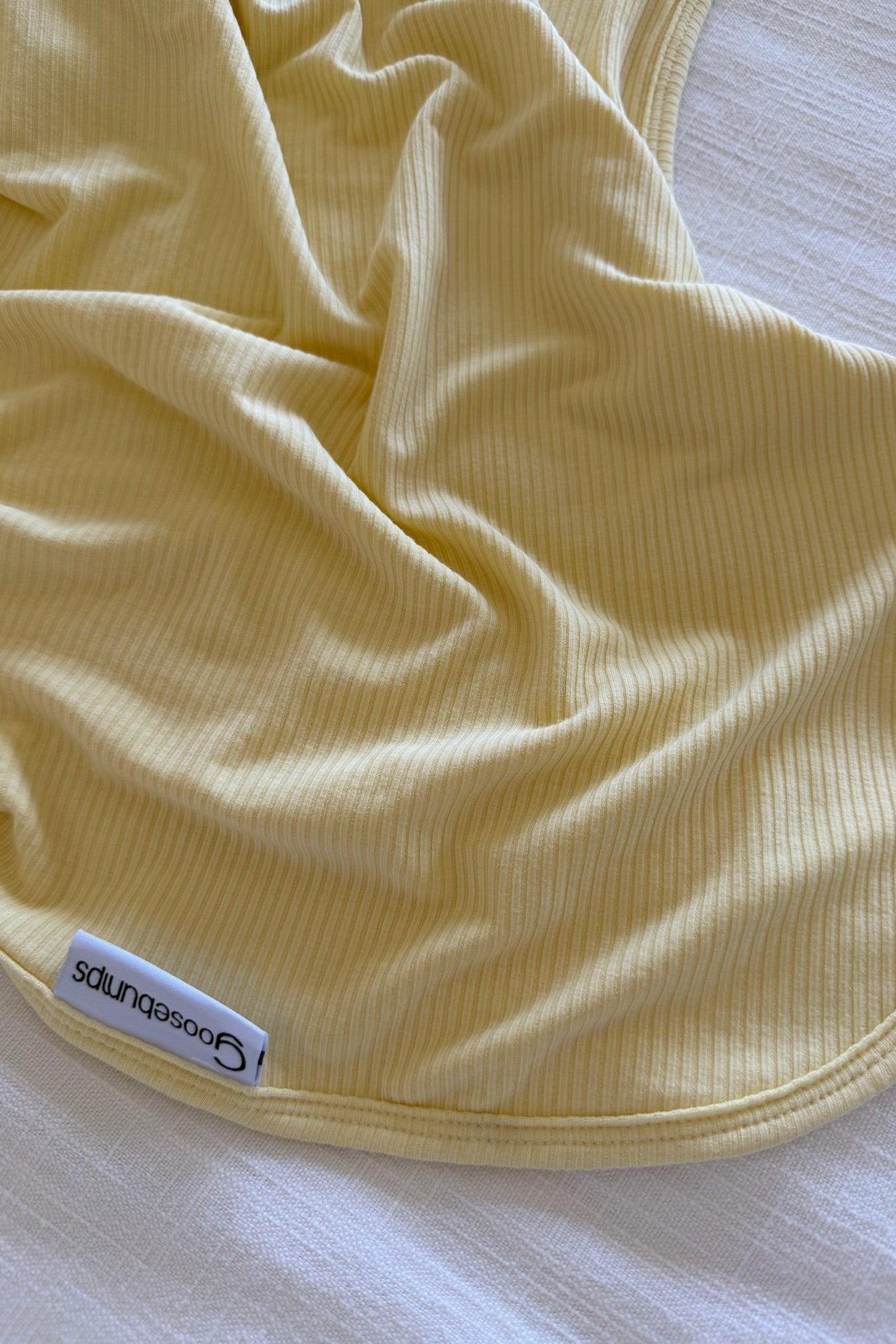 A butter-colored, ribbed bamboo blanket with a goosebumps label is spread out on a white textured surface.