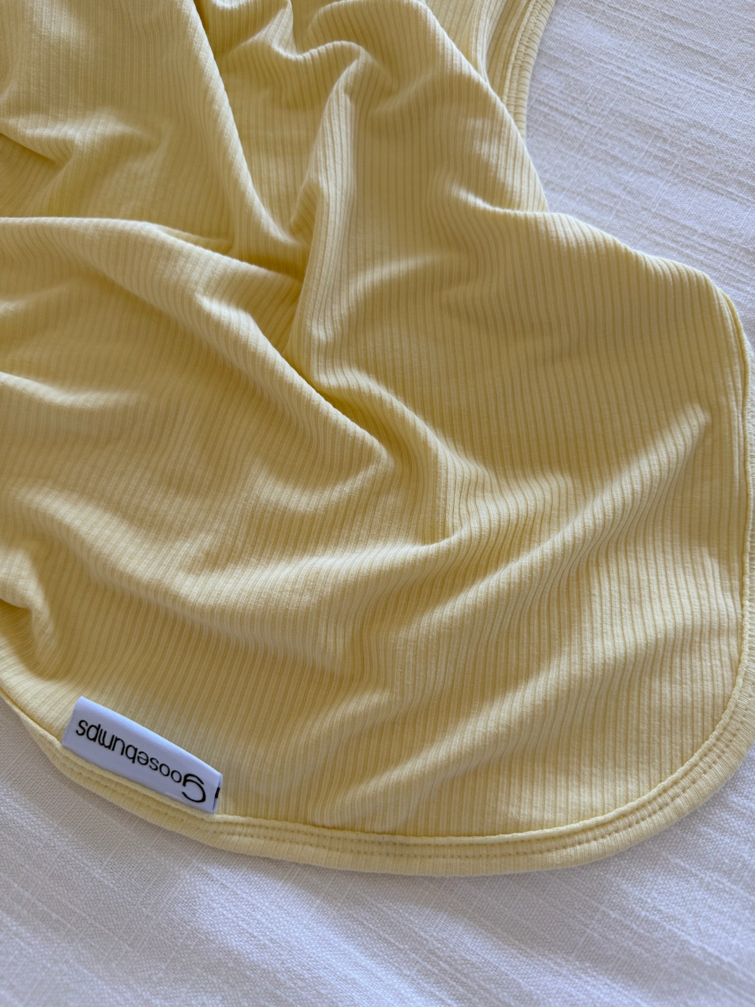 A butter-colored, ribbed bamboo blanket with a goosebumps label is spread out on a white textured surface.