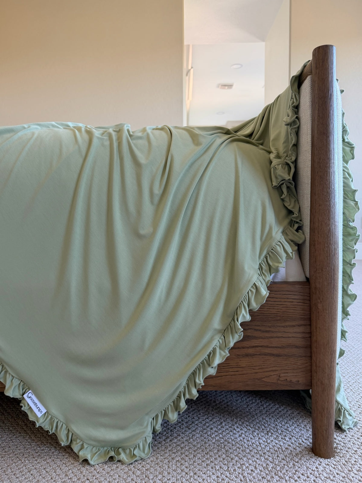Frosted fir / ruffle sage green bamboo blanket draped over a wooden bed frame.