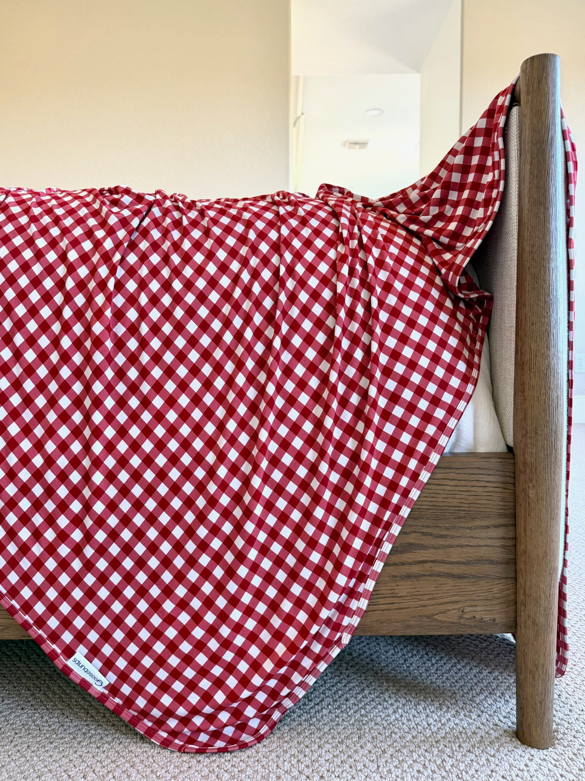 A red and white gingham ckeckin’ it twice bamboo blanket draped over the corner of a wooden bed frame.