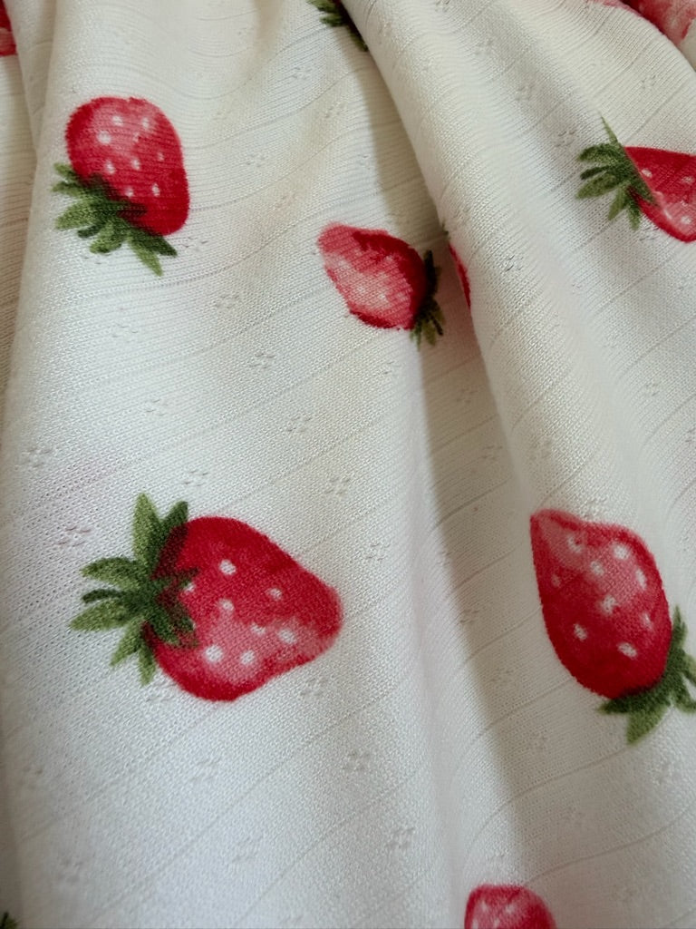 Close-up of the berries / pointelle fabric featuring a ribbed texture and repeating red strawberry and green leaf pattern. The soft material has gentle folds that create subtle shadows.