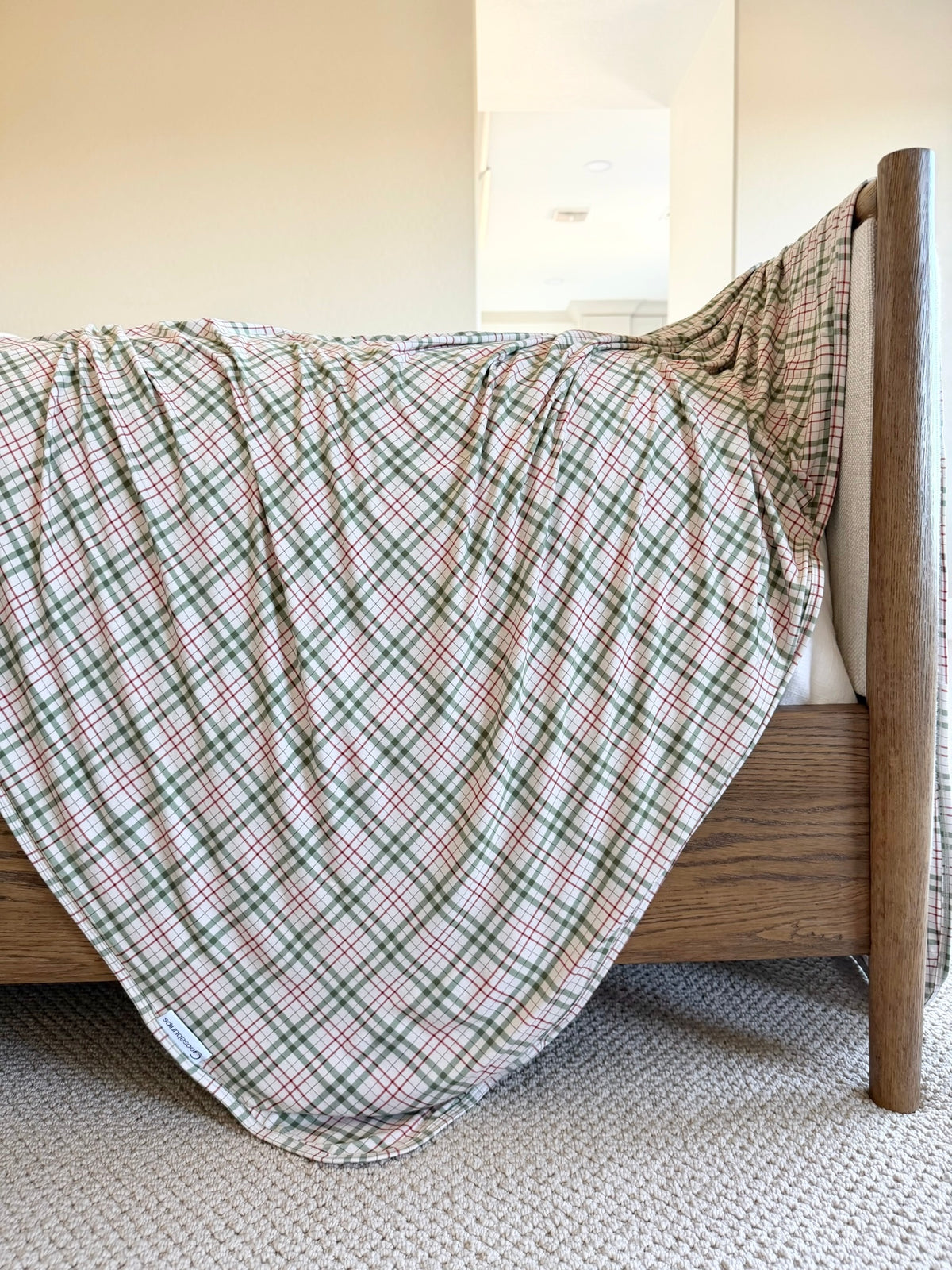 The homestead blanket, in luxurious shades of green, red, and cream, is draped over the corner of a wooden bed frame.