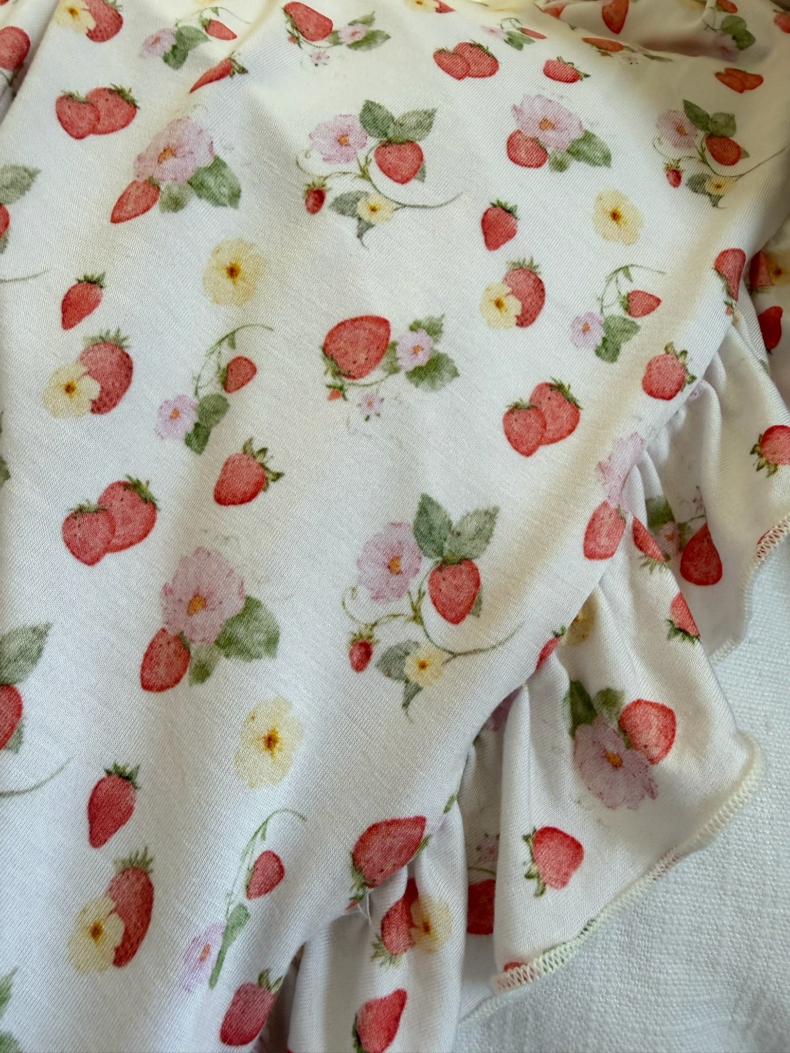 The "freshly picked / ruffle" blanket features soft white fabric with red strawberries, pastel flowers, and green leaves, draped to display delicate ruffled edges.