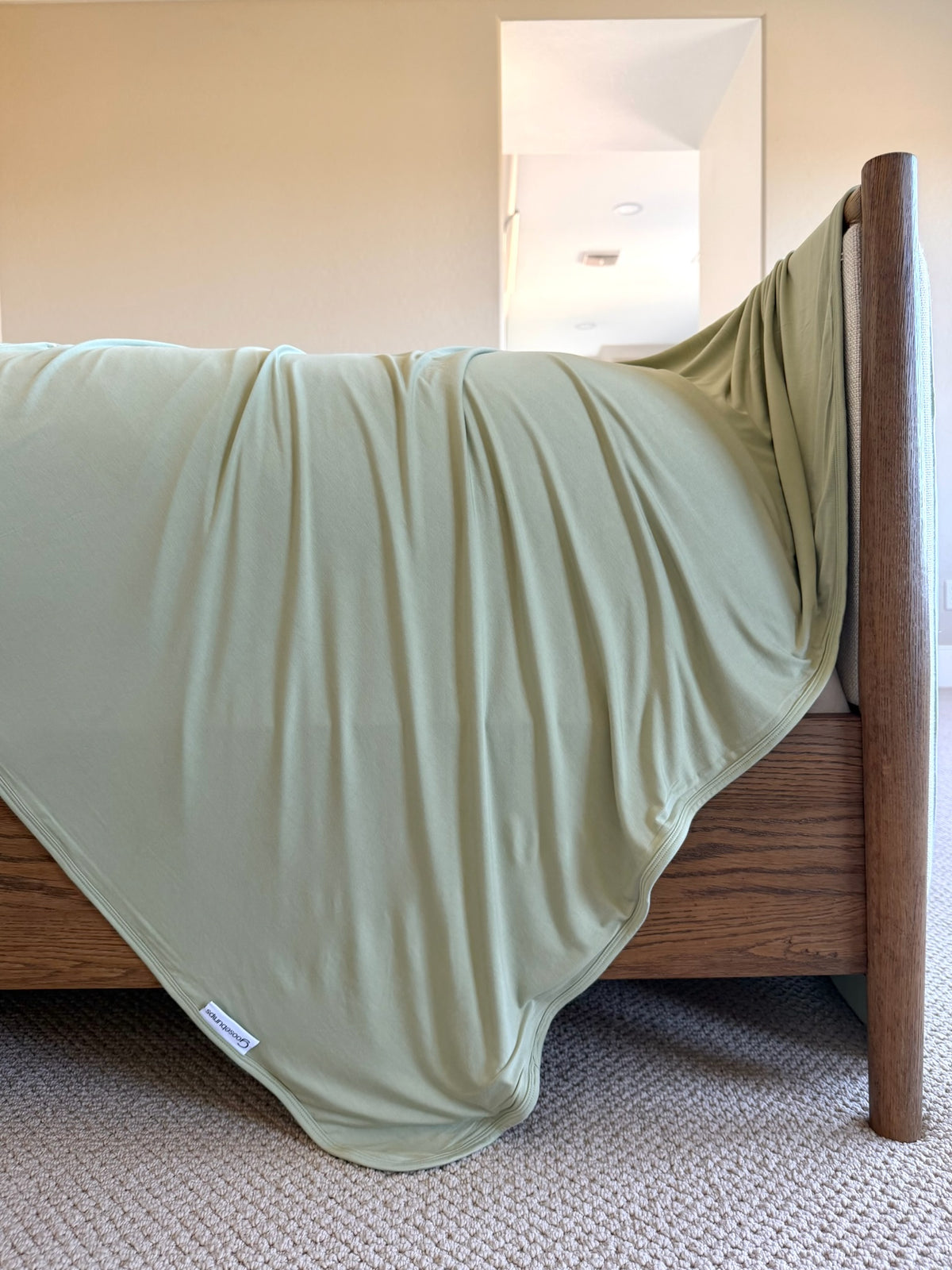 A luxurious sage green frosted fir bamboo blanket draped over the foot of a wooden bed frame.