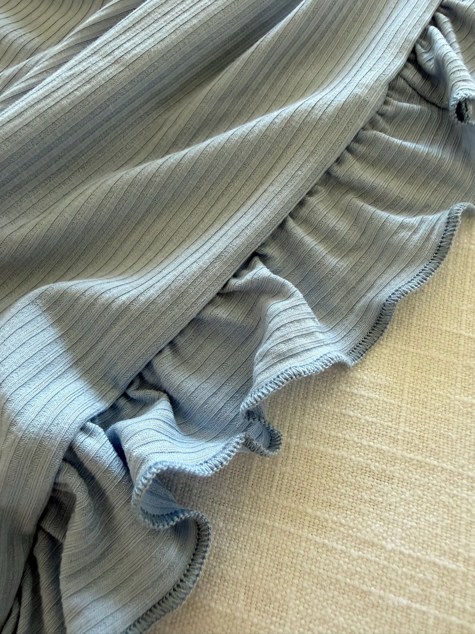 A close-up of the cove ribbed ruffle blanket in light blue, featuring ruffled edges and a ribbed texture, draped over a beige surface.