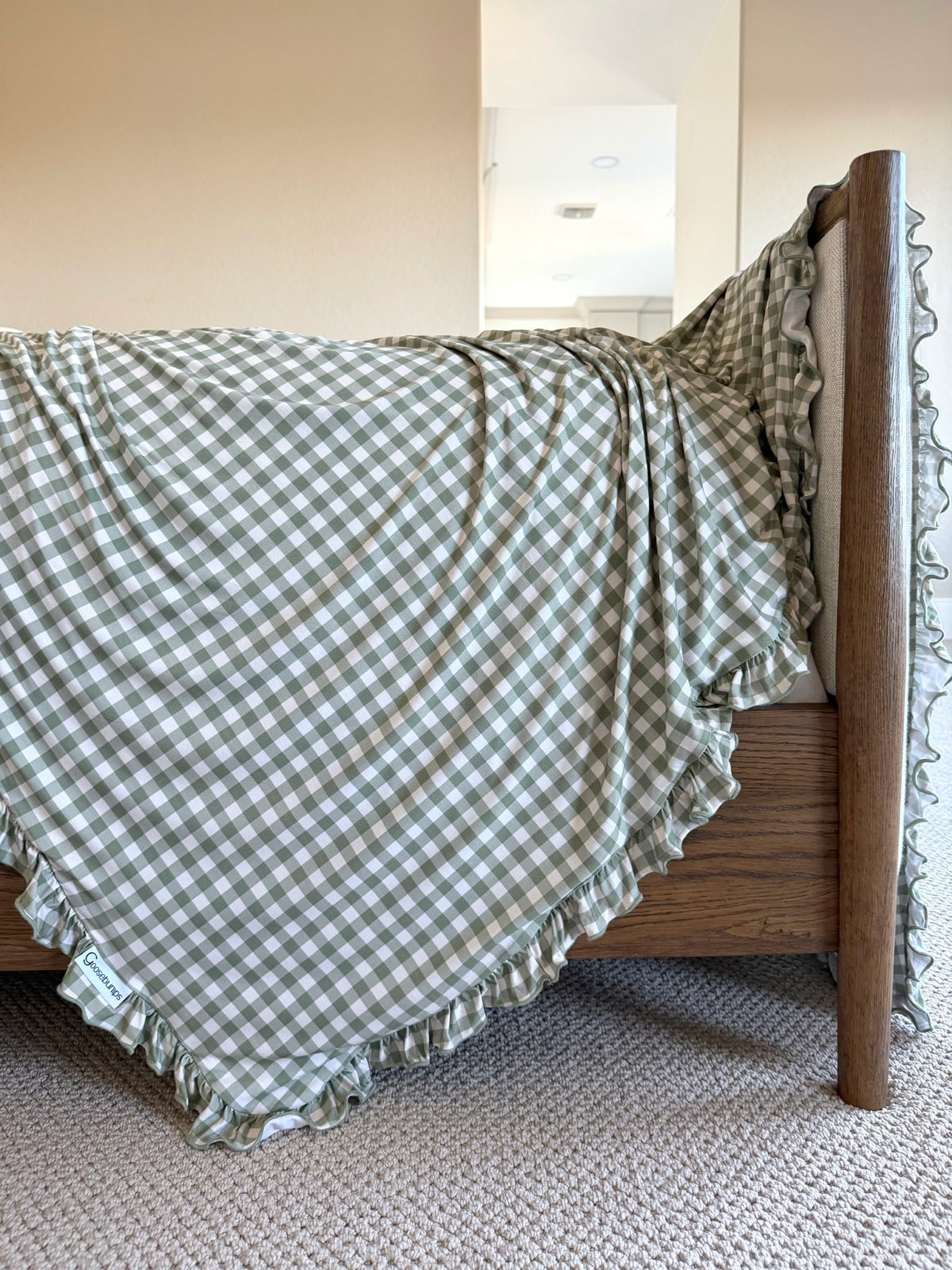 Evergreen lane / ruffle luxurious green and ivory gingham bamboo blanket with a ruffled edge draped over a wooden bed frame.
