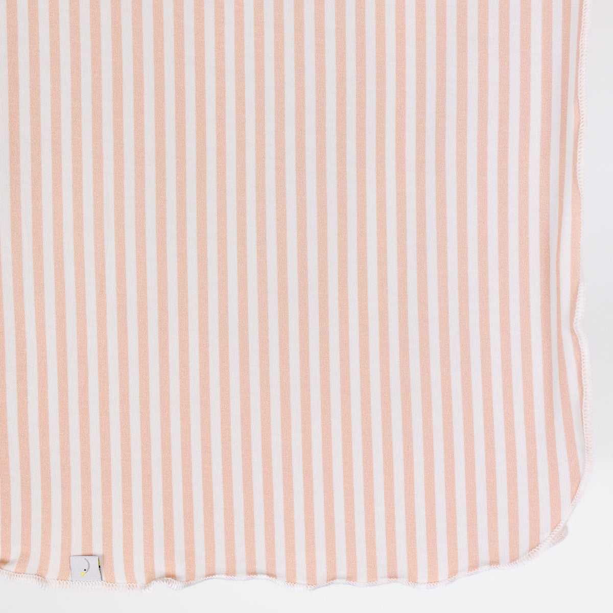 A close-up of the heritage / swaddle, featuring pink and ivory vertical stripes, a rounded, slightly scalloped edge, and a small fabric tag visible at the bottom left corner.