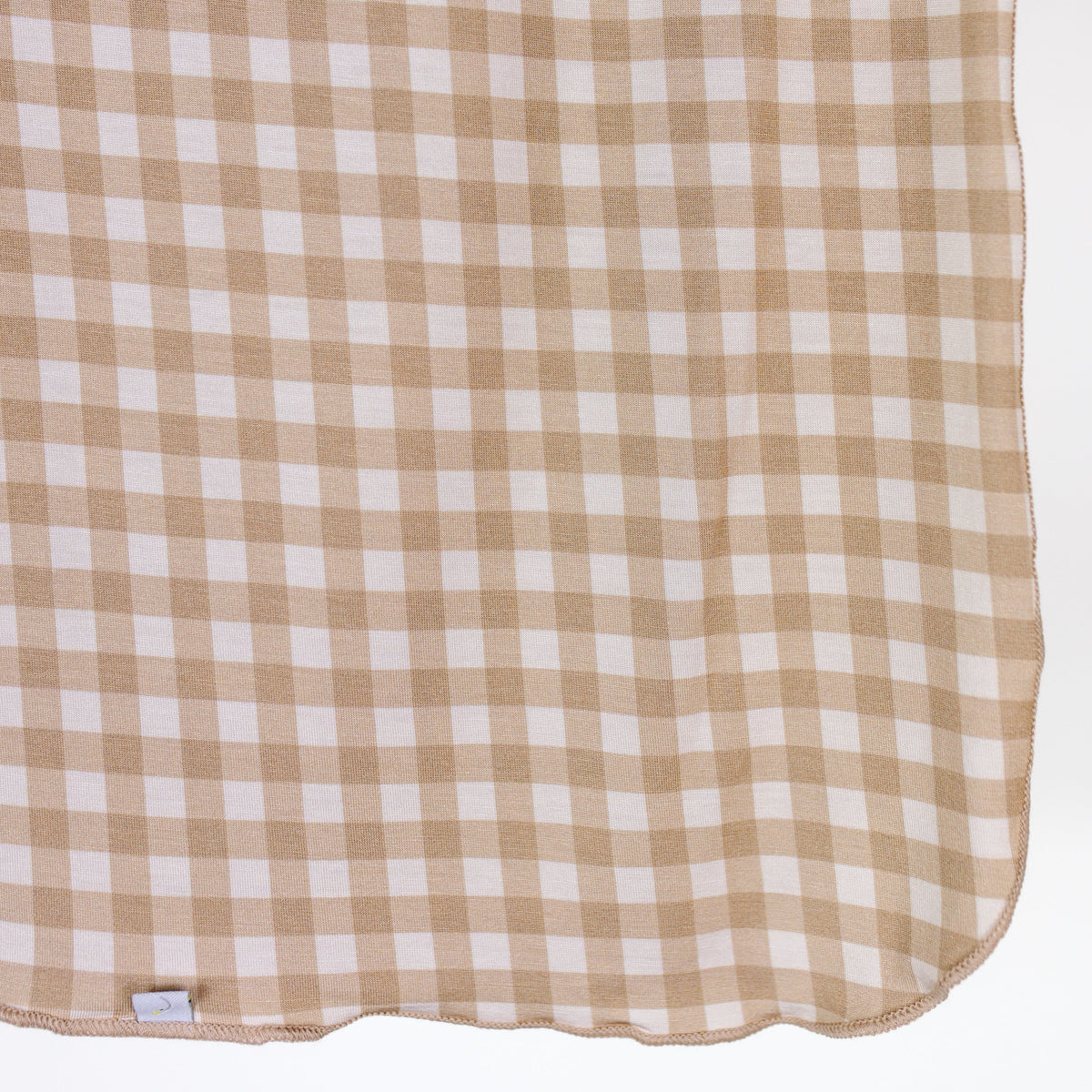 The teddy bear check / swaddle features a beige and white gingham-patterned, lightweight single layer fabric draped gracefully with a small gray tag at the bottom edge, set against a plain white background—perfect for keeping your little one cozy.