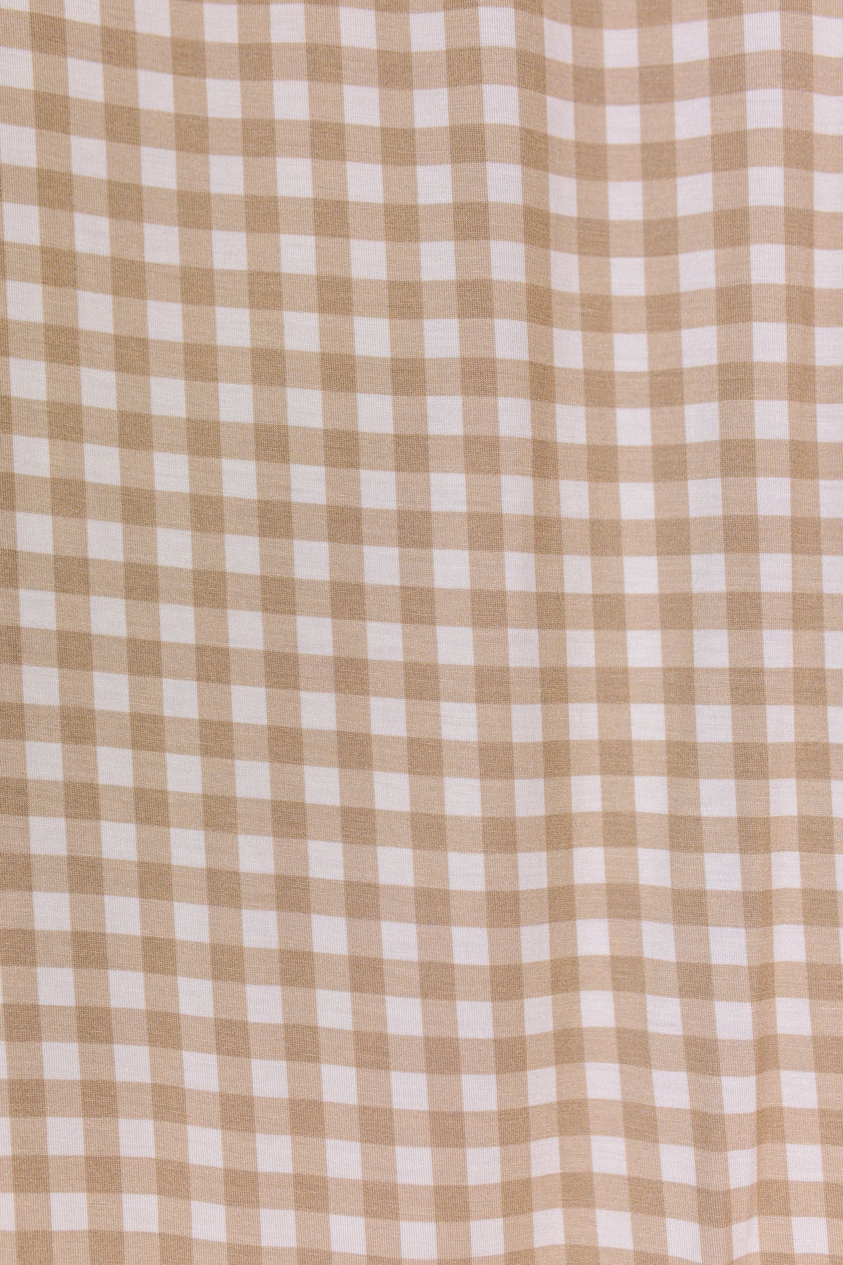 Sure! Here’s a rewritten version using your product data: The teddy bear check / swaddle features tan and white gingham fabric with a small checked pattern, perfect for creating a timeless swaddle. This single layer material drapes softly, with subtle folds that cast gentle shadows and highlights across its surface.
