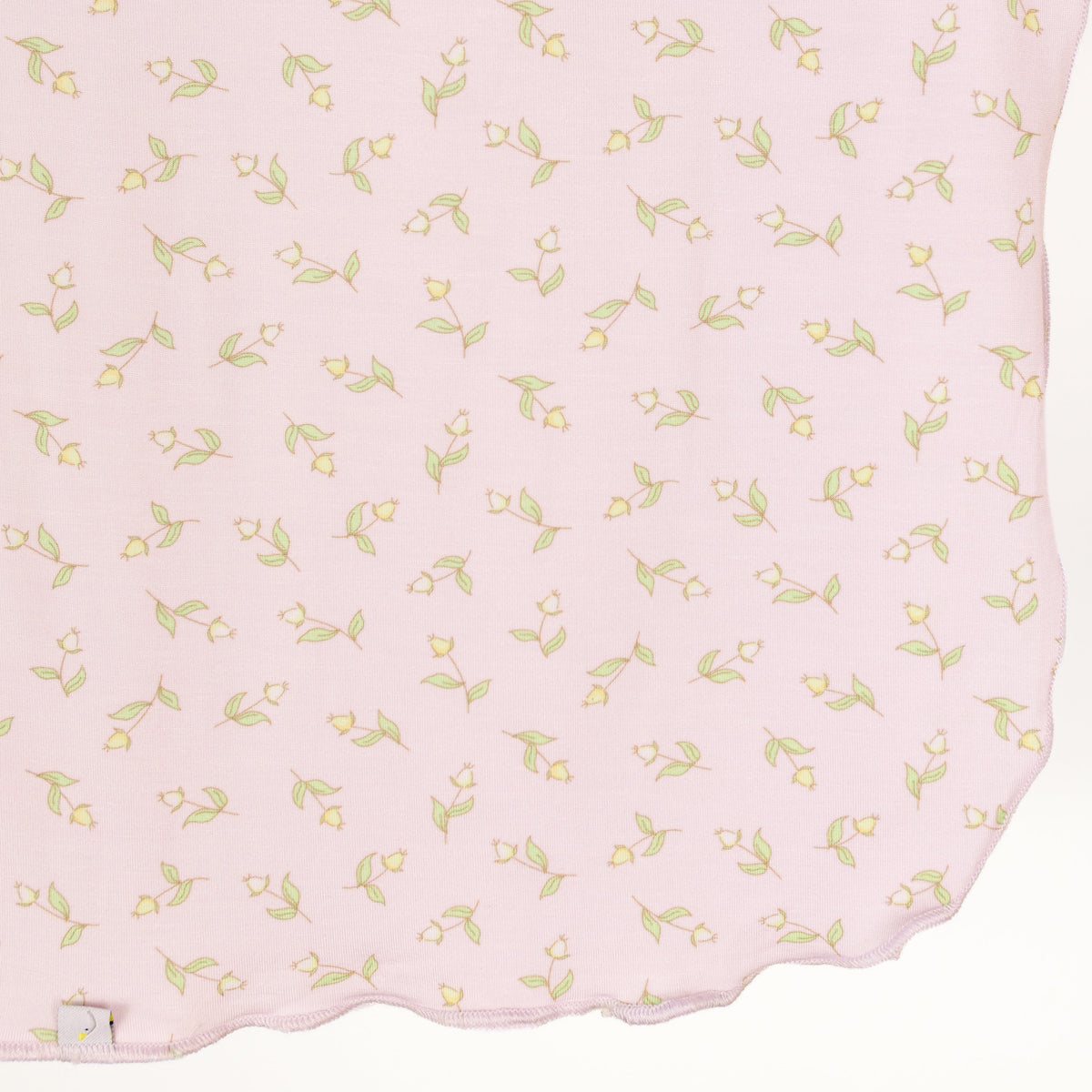 Crafted from light pink fabric adorned with small yellow flowers and green leaves, the rosebud / swaddle features a wavy scalloped edge along the bottom, making it a charming pink baby blanket for your little one.
